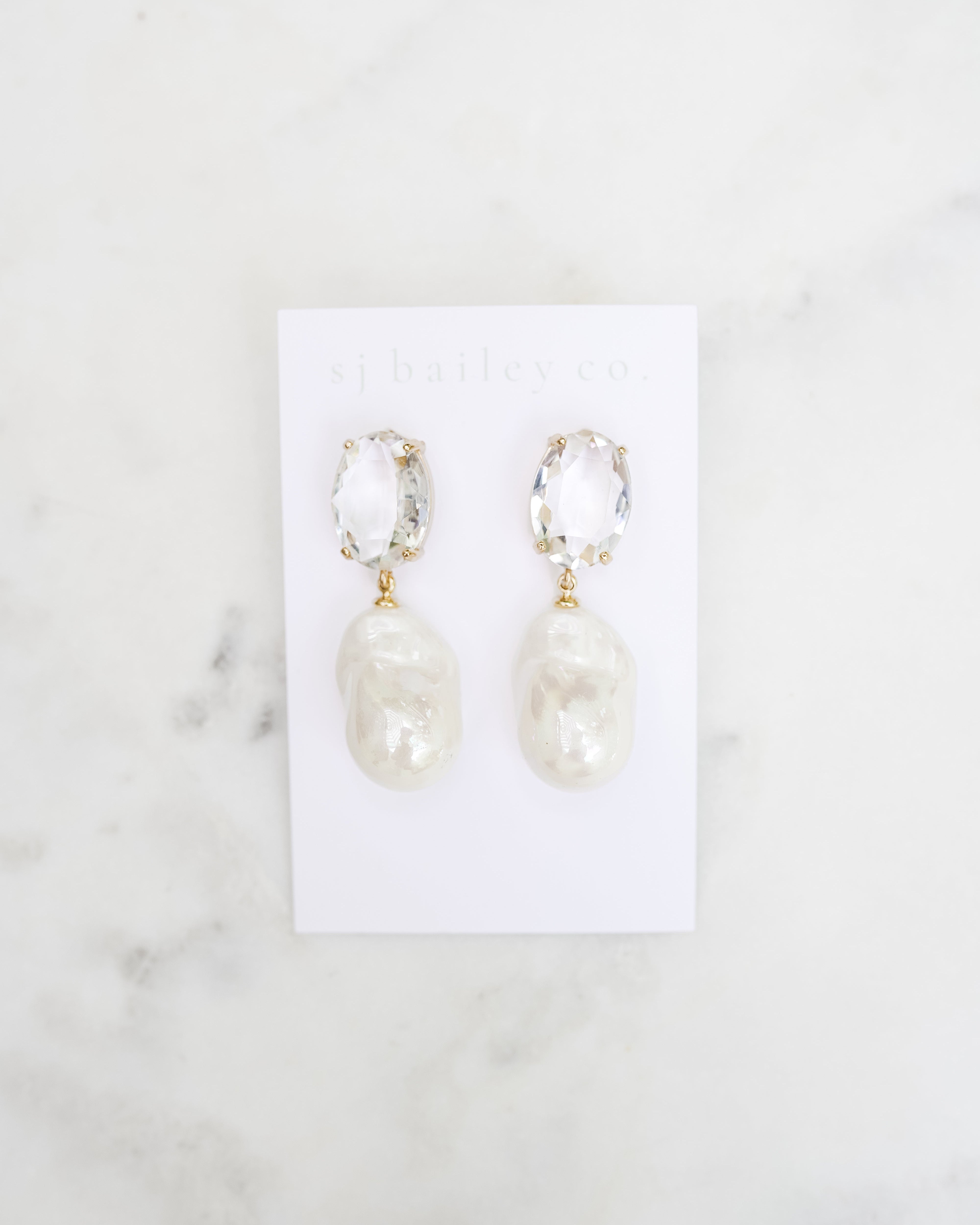 Crystal Oval and pearl pendant earrings on a white marble background.