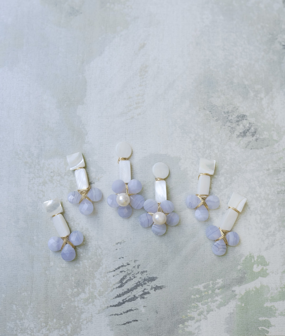 mother of pearl and blue lace agate statement earrings on a green floral wallpaper background