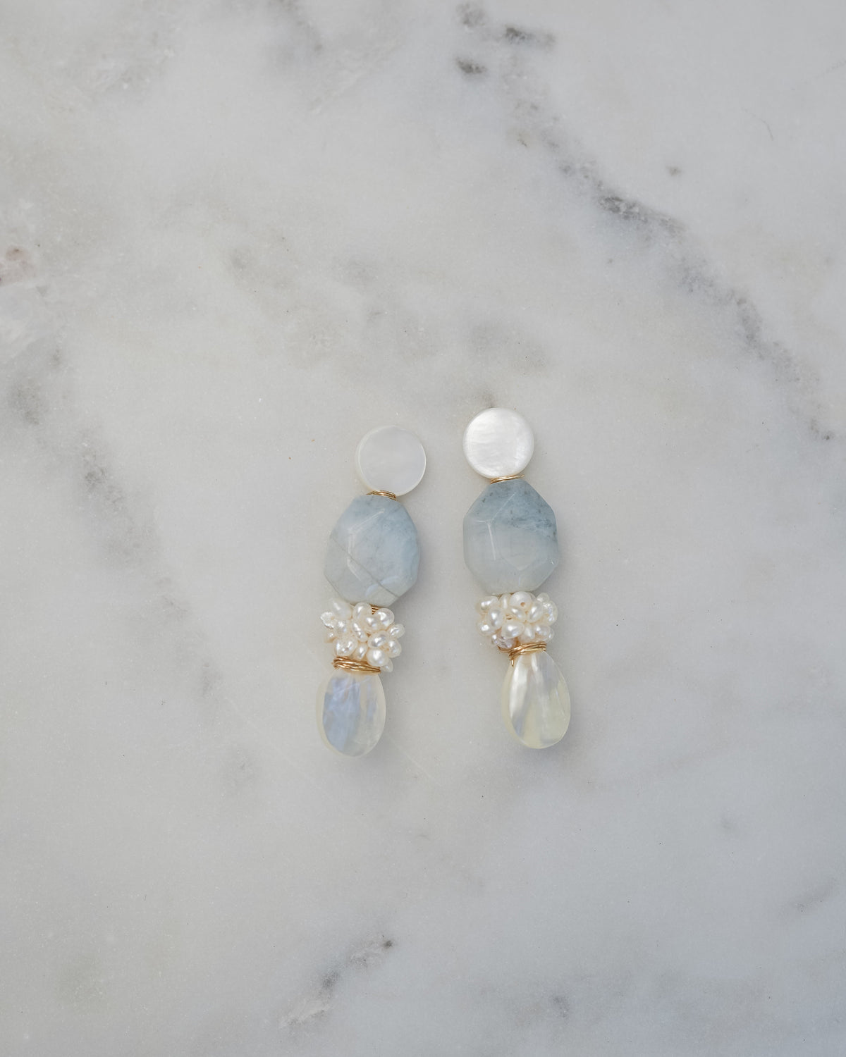 mother of pearl and aquamarine statement earrings on a white marble background