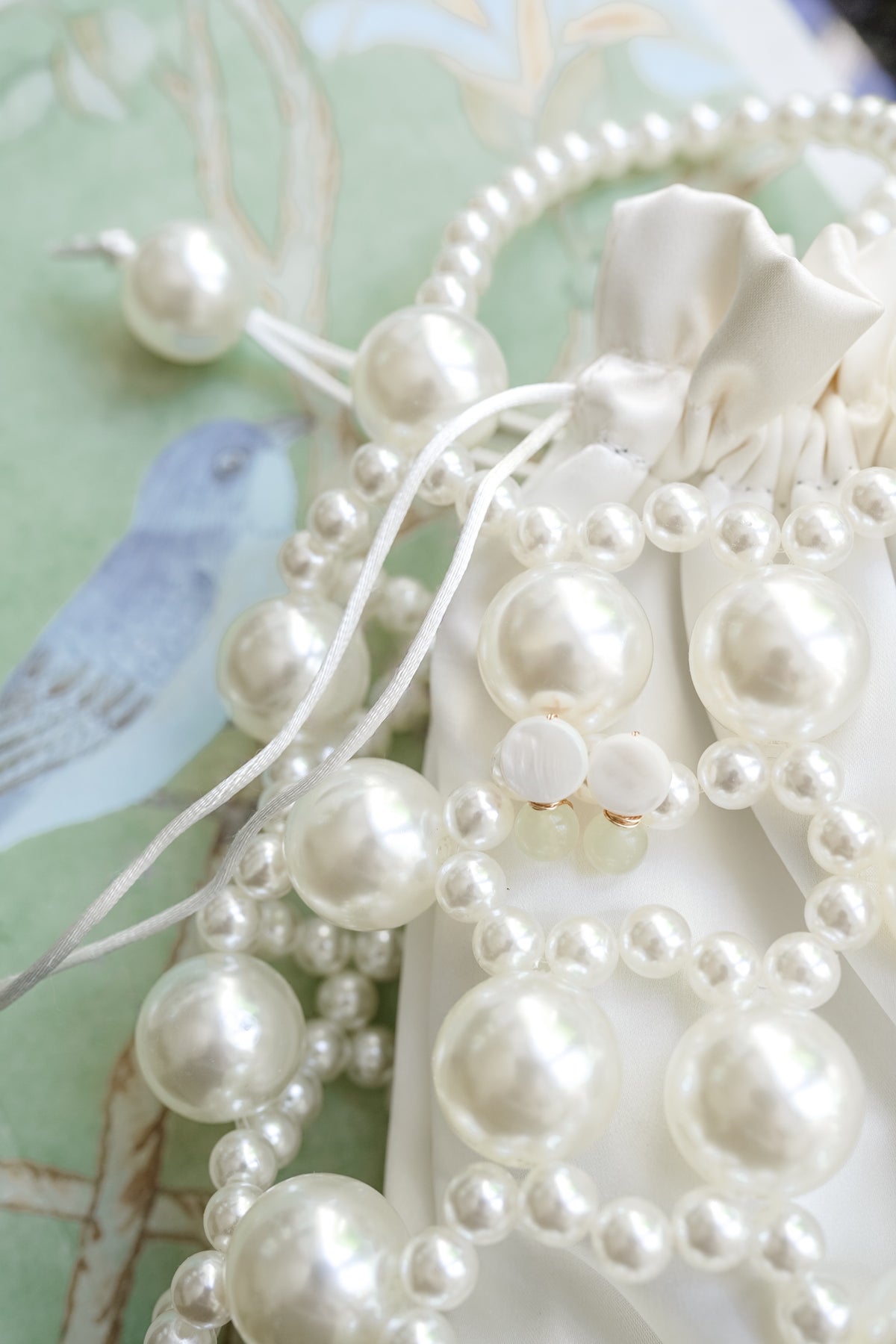 White and green mother of pearl earrings resting on a white faux-pearl beaded purse against a little green and blue chinoiserie background.