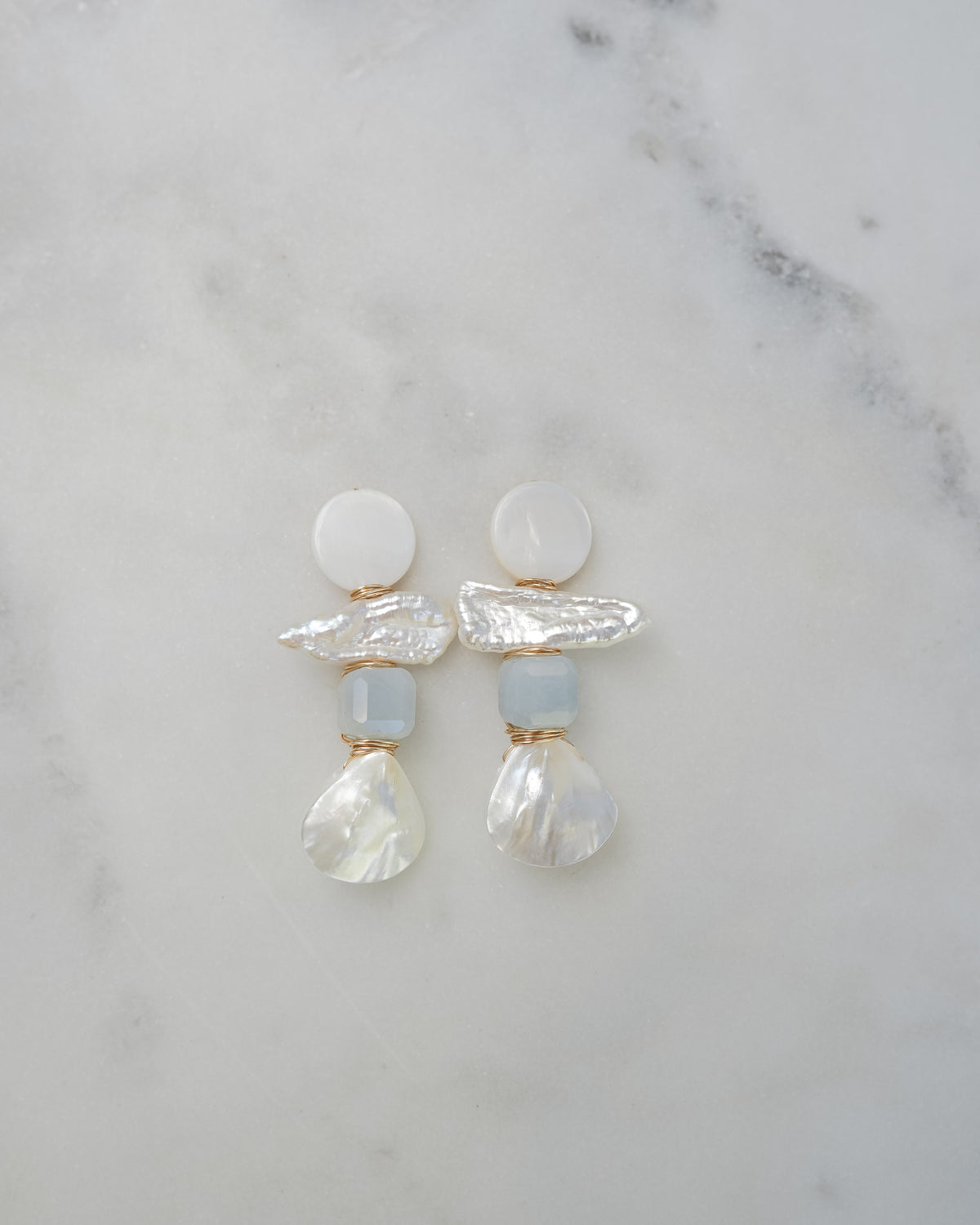 mother of pearl and aquamarine statement earrings on a white marble background