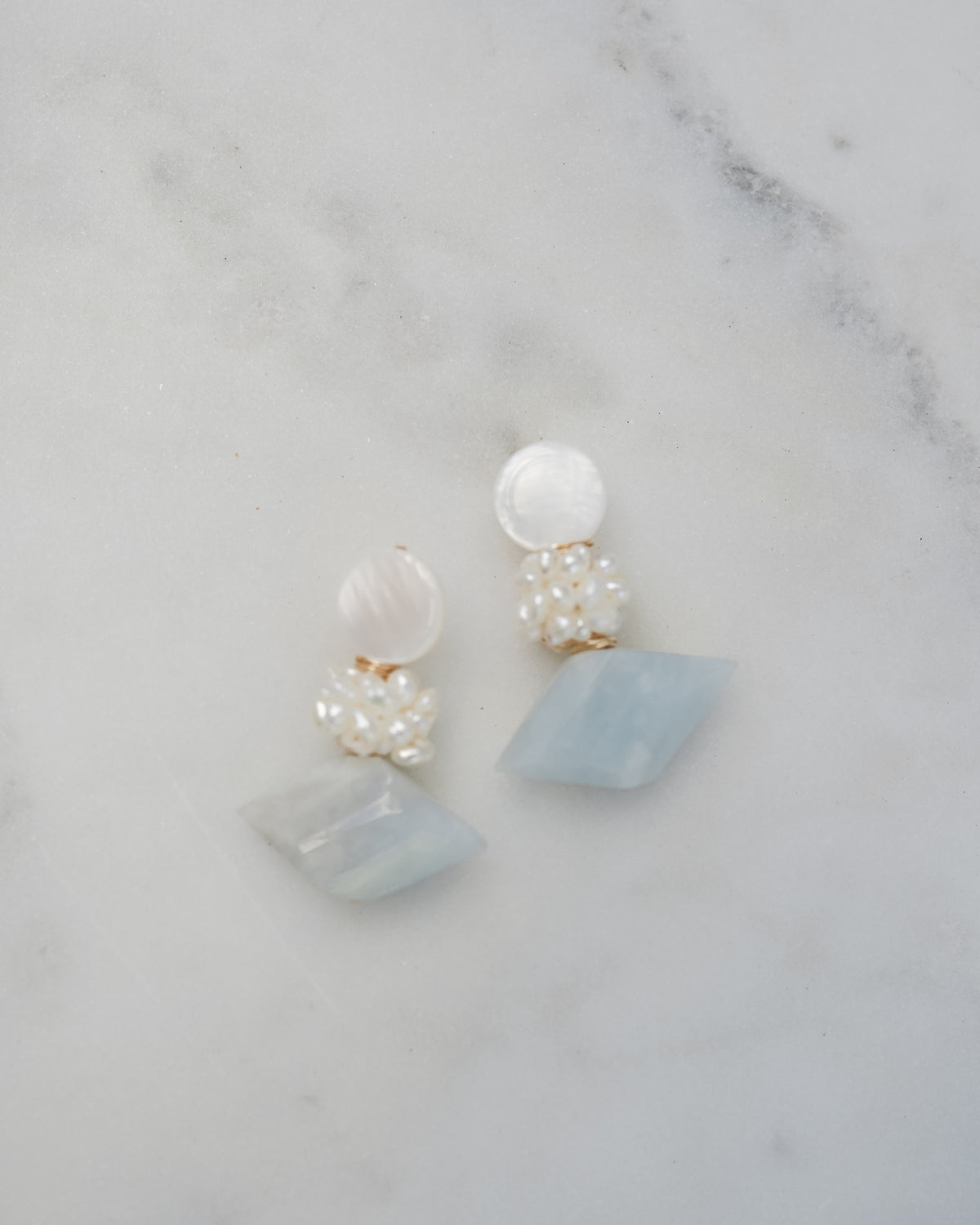 mother of pearl and aquamarine statement earrings on a white marble background