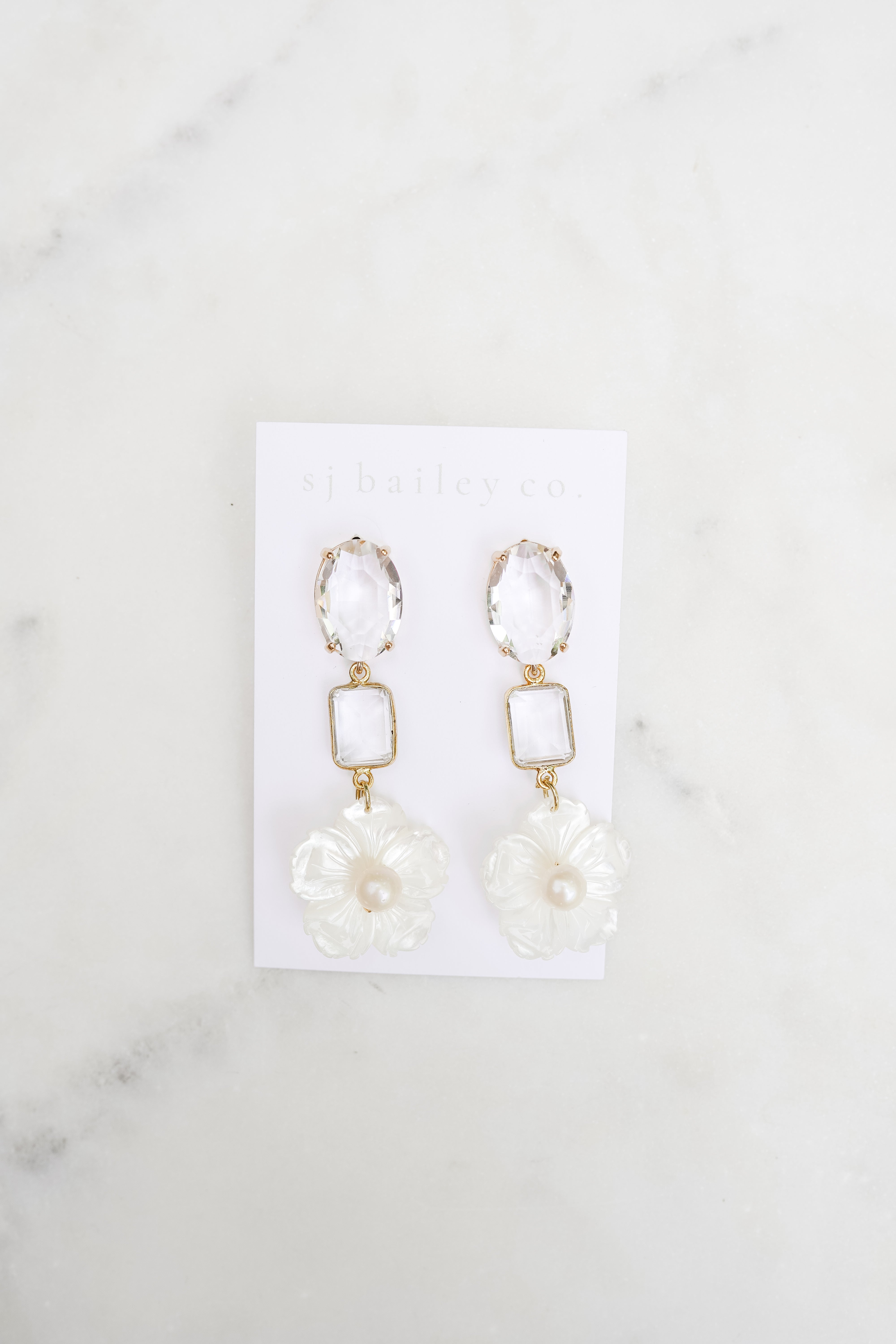 Pair of earrings on a white card with a marble background