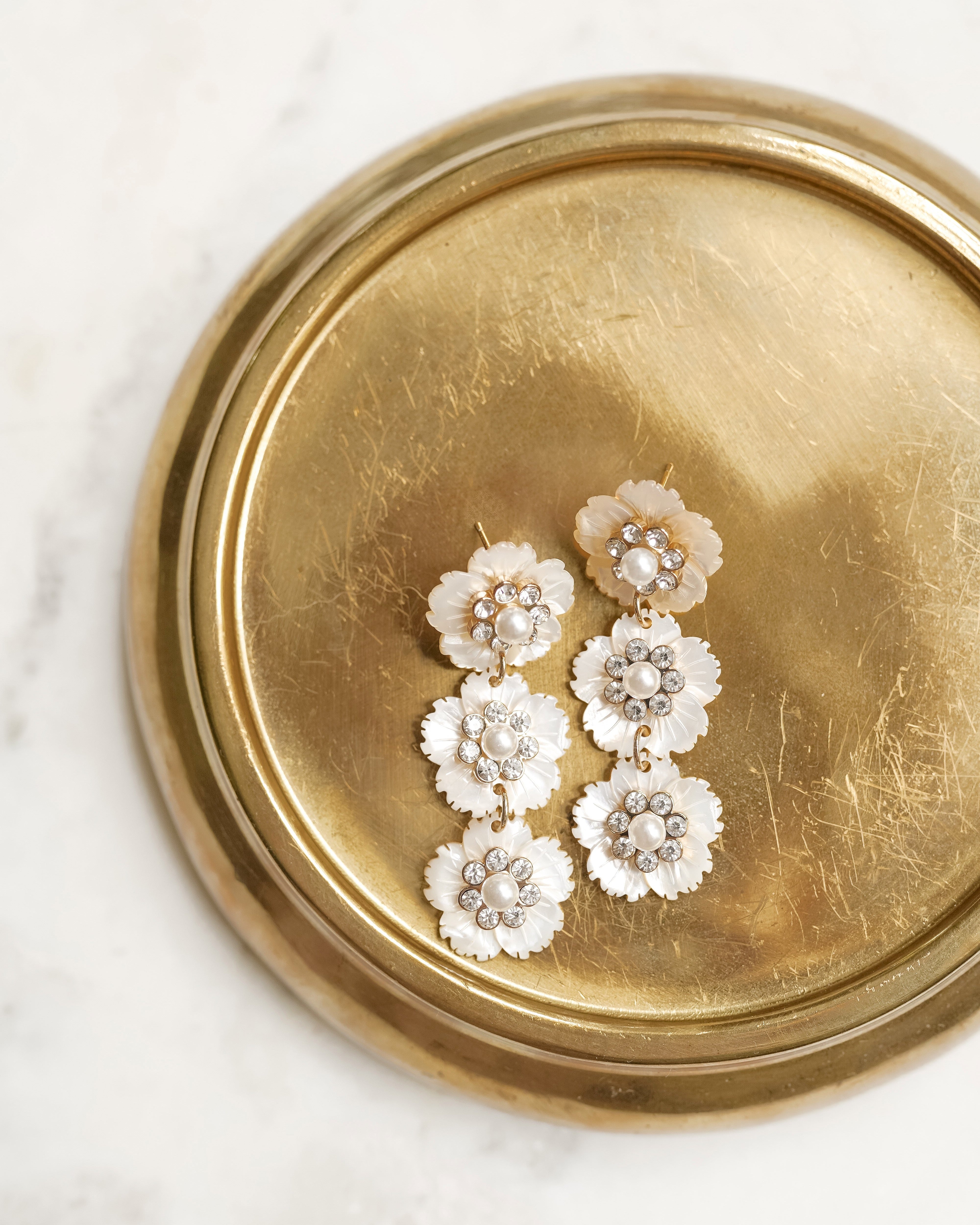 White floral stud earrings on a brass tray on a marble background