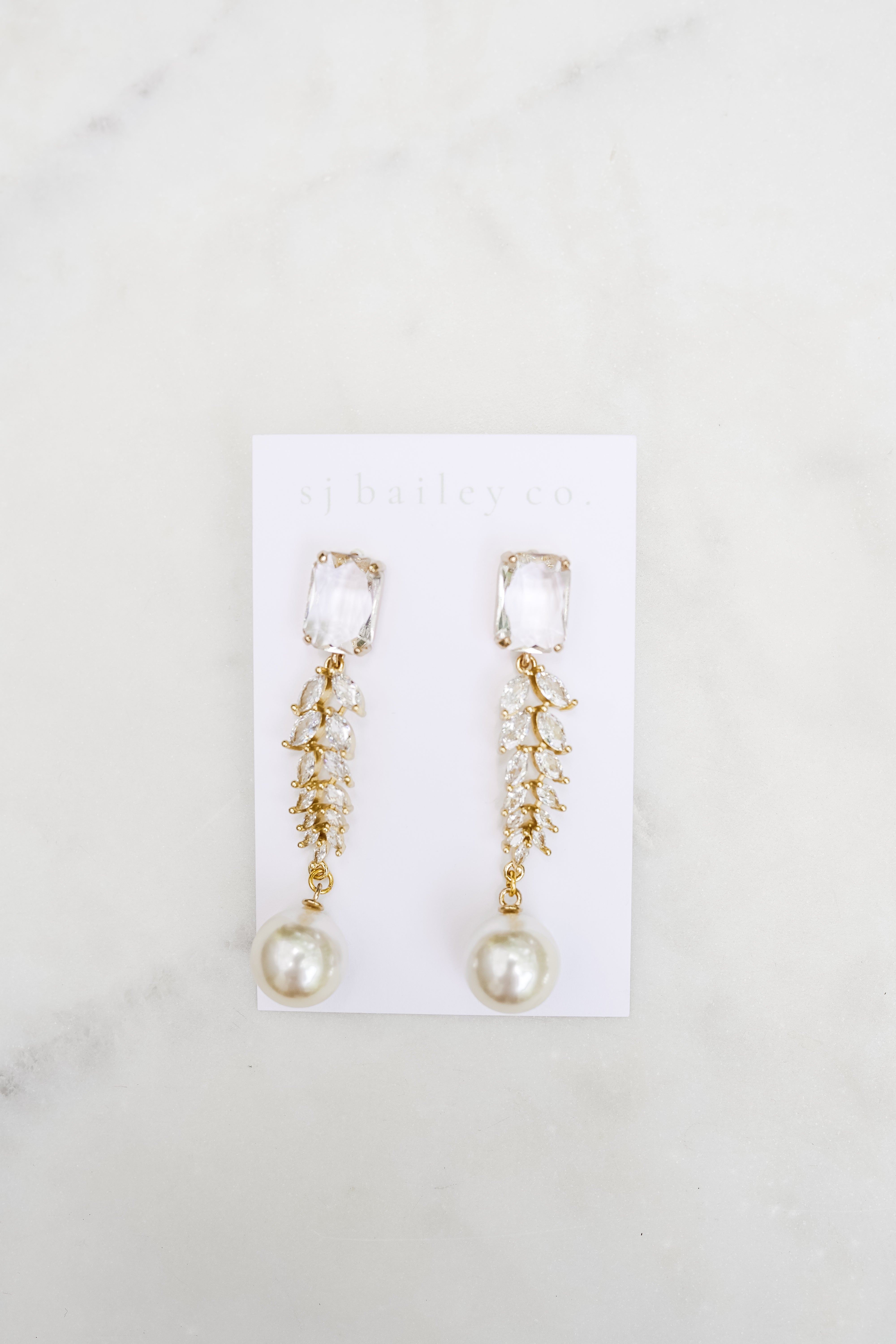 Crystal and pearl statement earrings on a white card on a marble background.