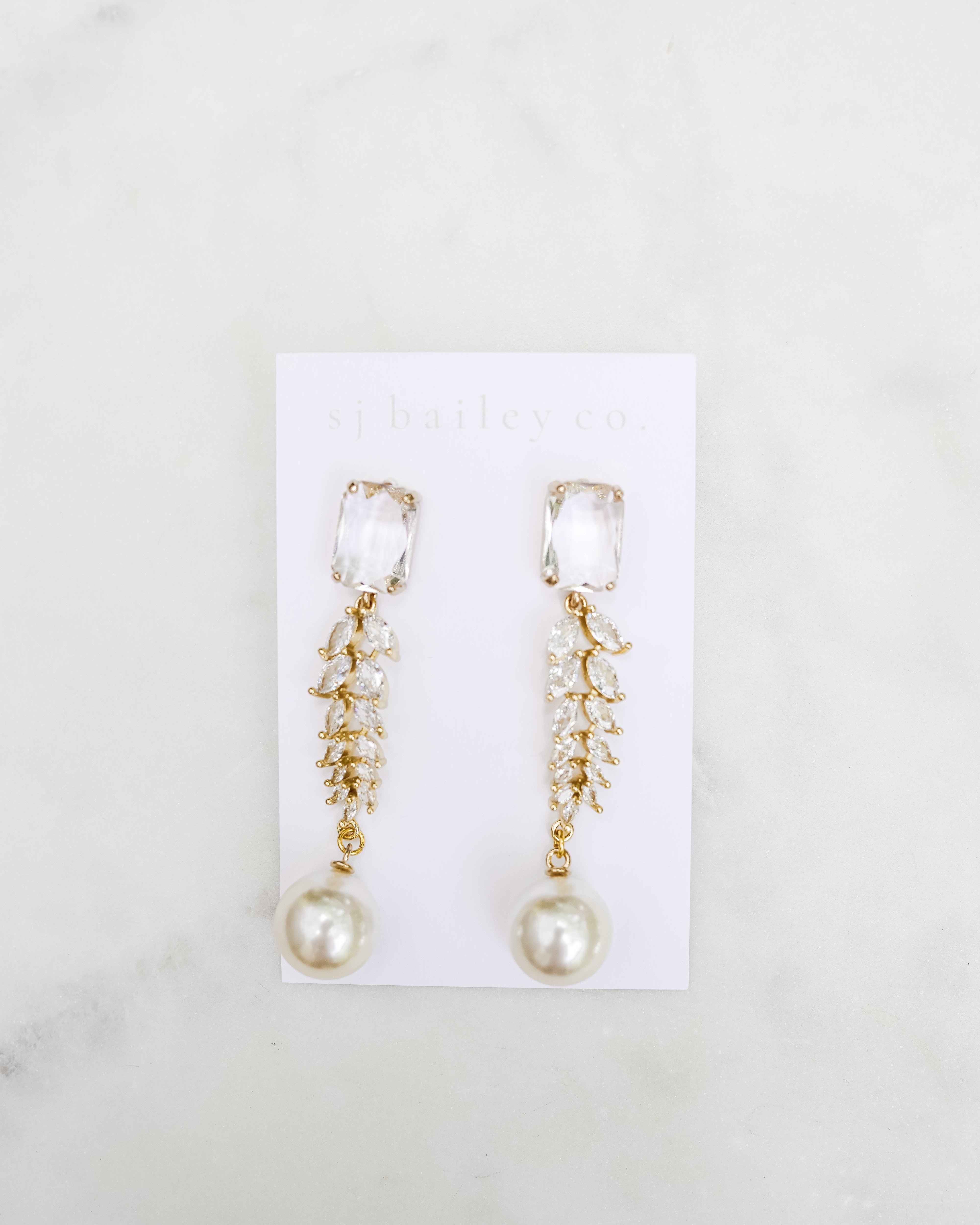 Crystal and pearl statement earrings on a white card on a marble background.