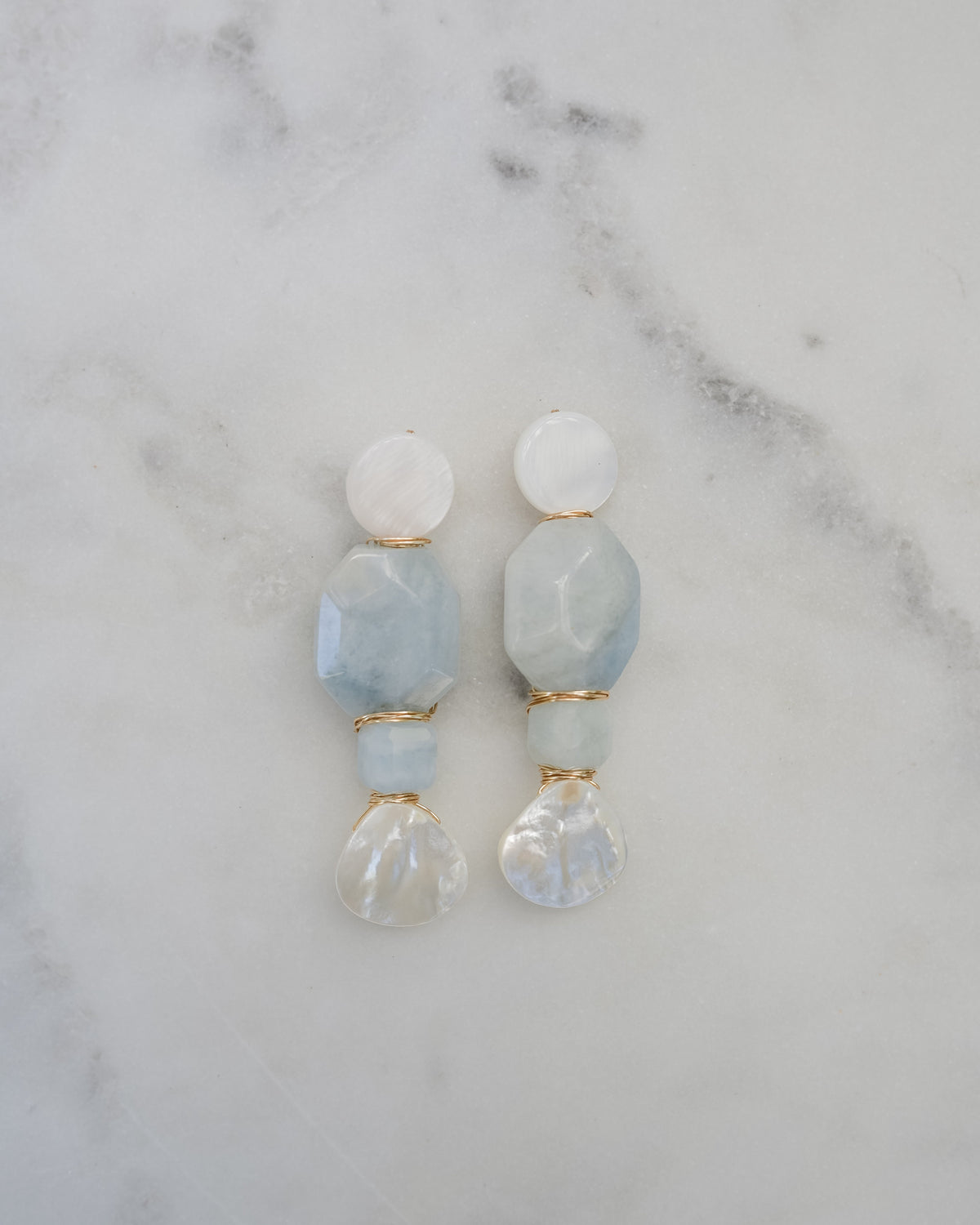 mother of pearl and aquamarine statement earrings on a white marble background