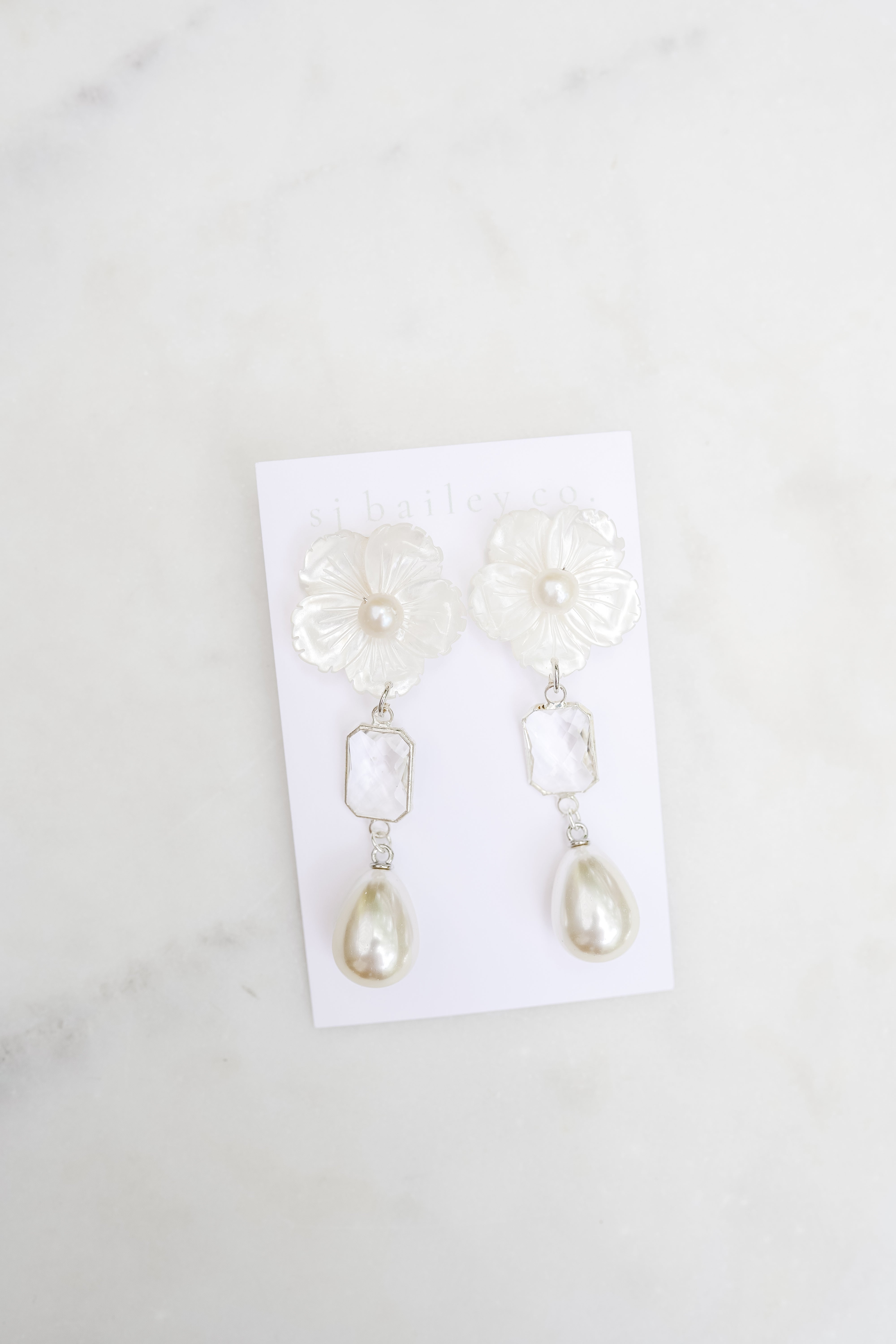 Pearl earrings on a white card with a marble background