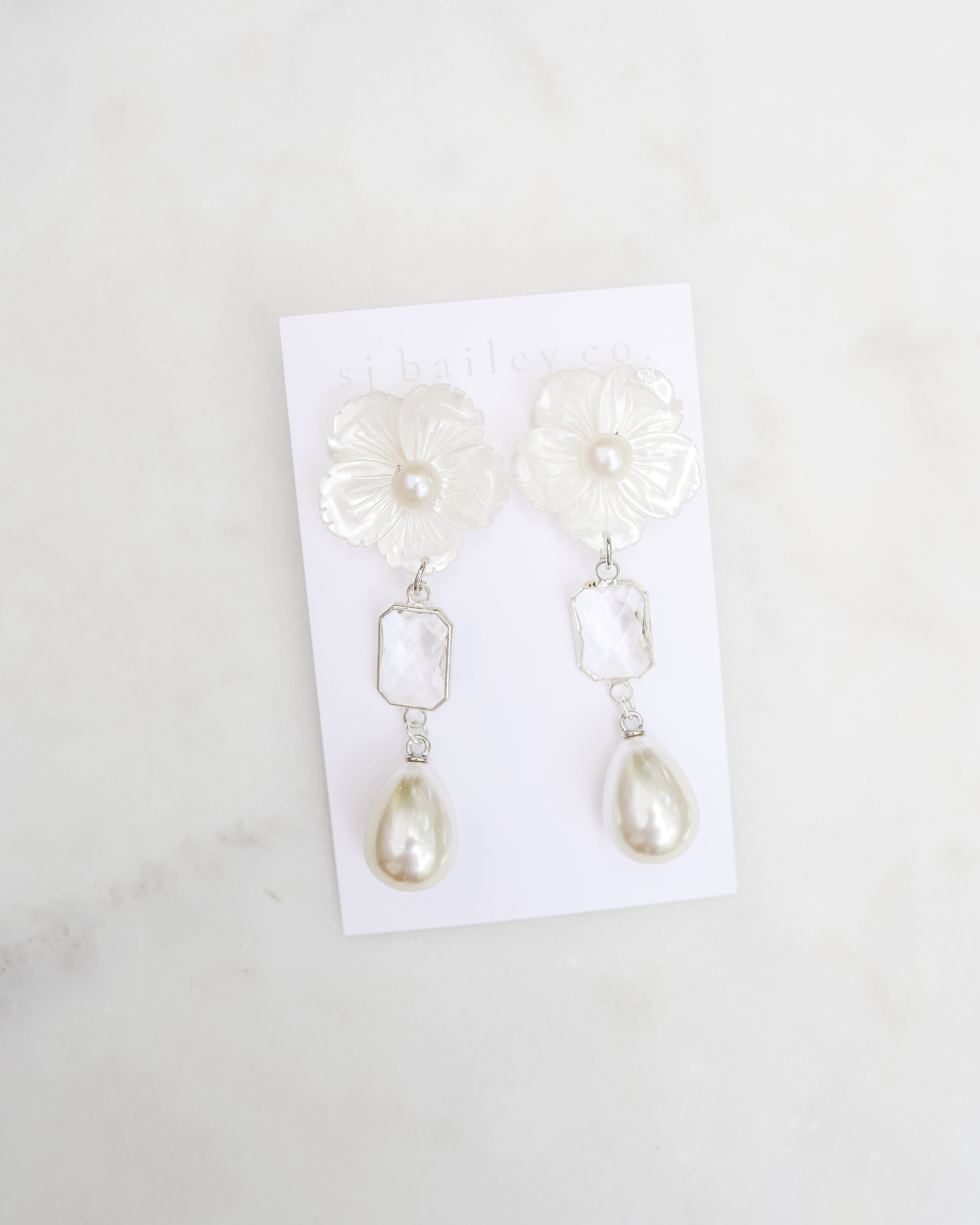 Pearl earrings on a white card with a marble background