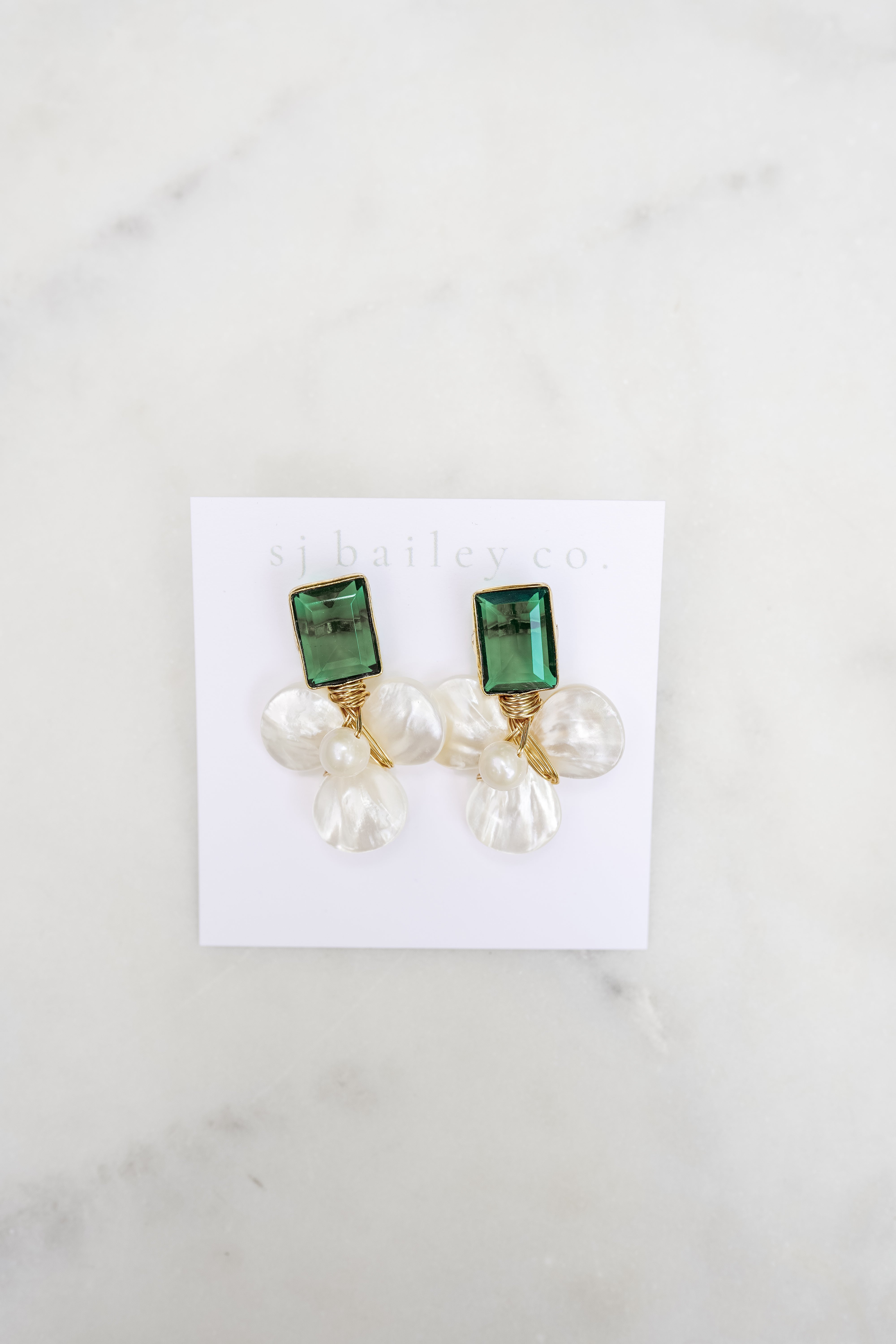 Dark emerald green and pearl earrings on a white card against a marble background.