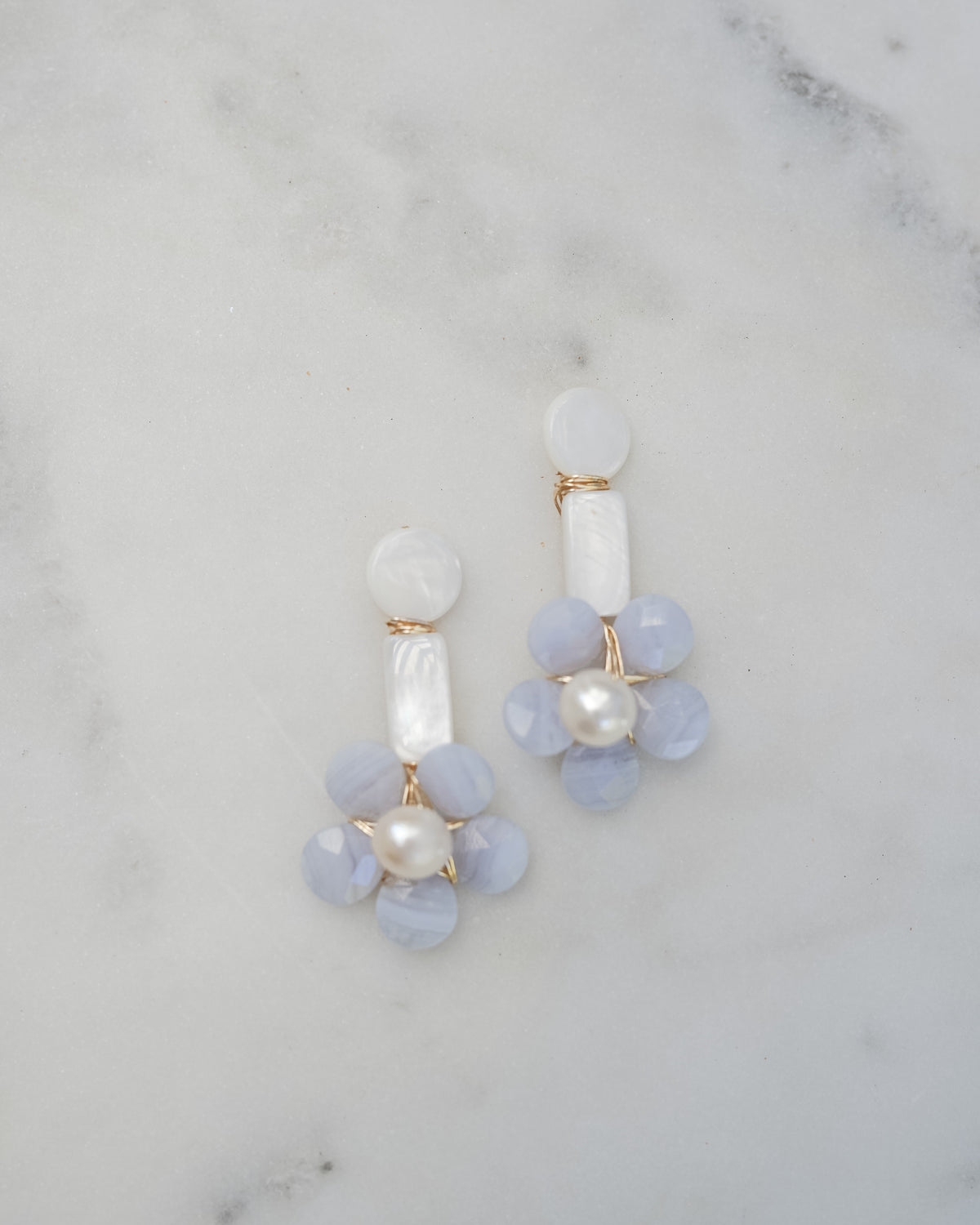 mother of pearl and blue lace agate floral statement earrings on a white marble background