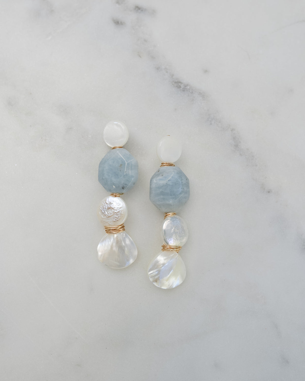 mother of pearl and aquamarine statement earrings on a white marble background