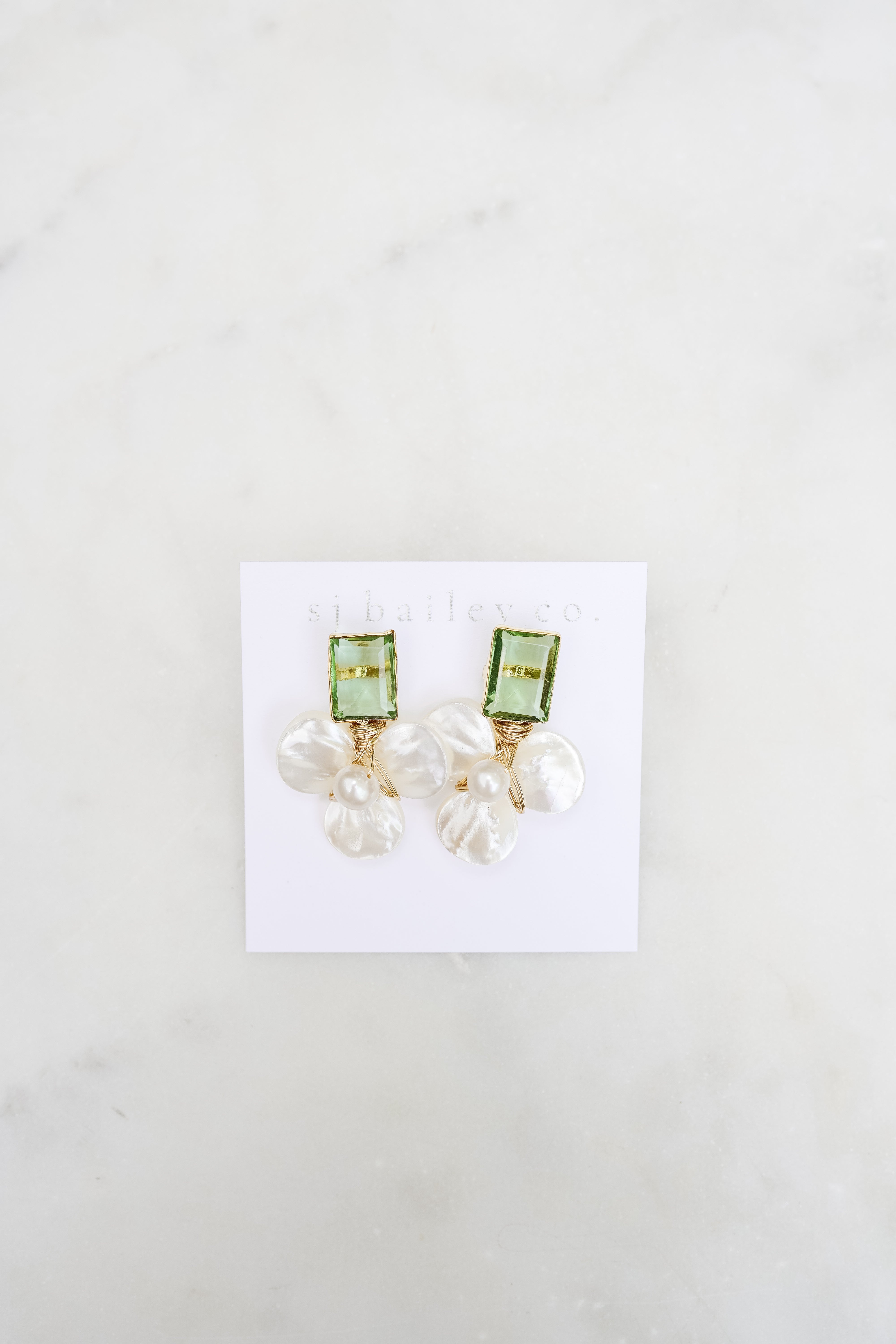 Peridot green and pearl earrings against a white card on a marble background.