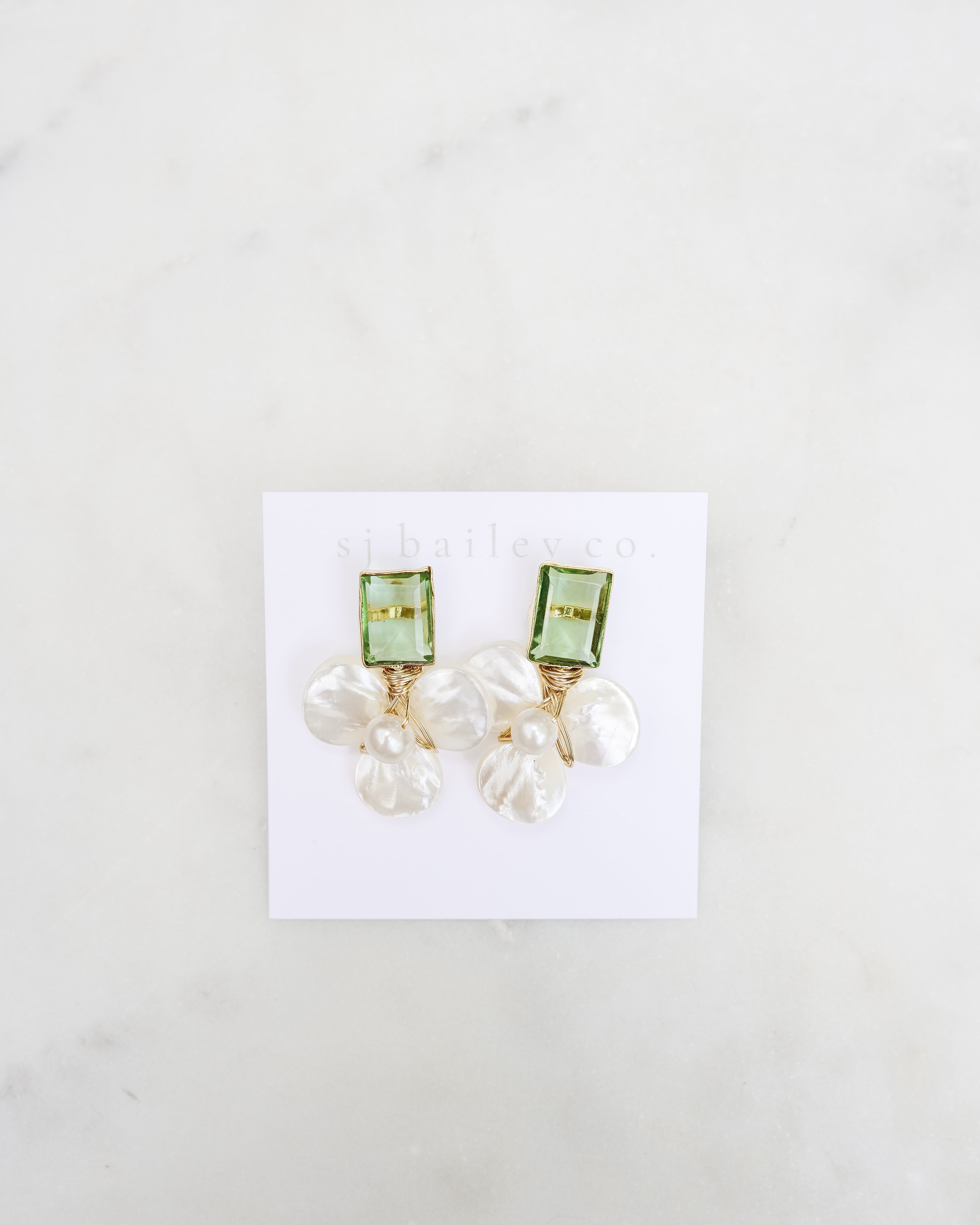 Peridot green and pearl earrings against a white card on a marble background.
