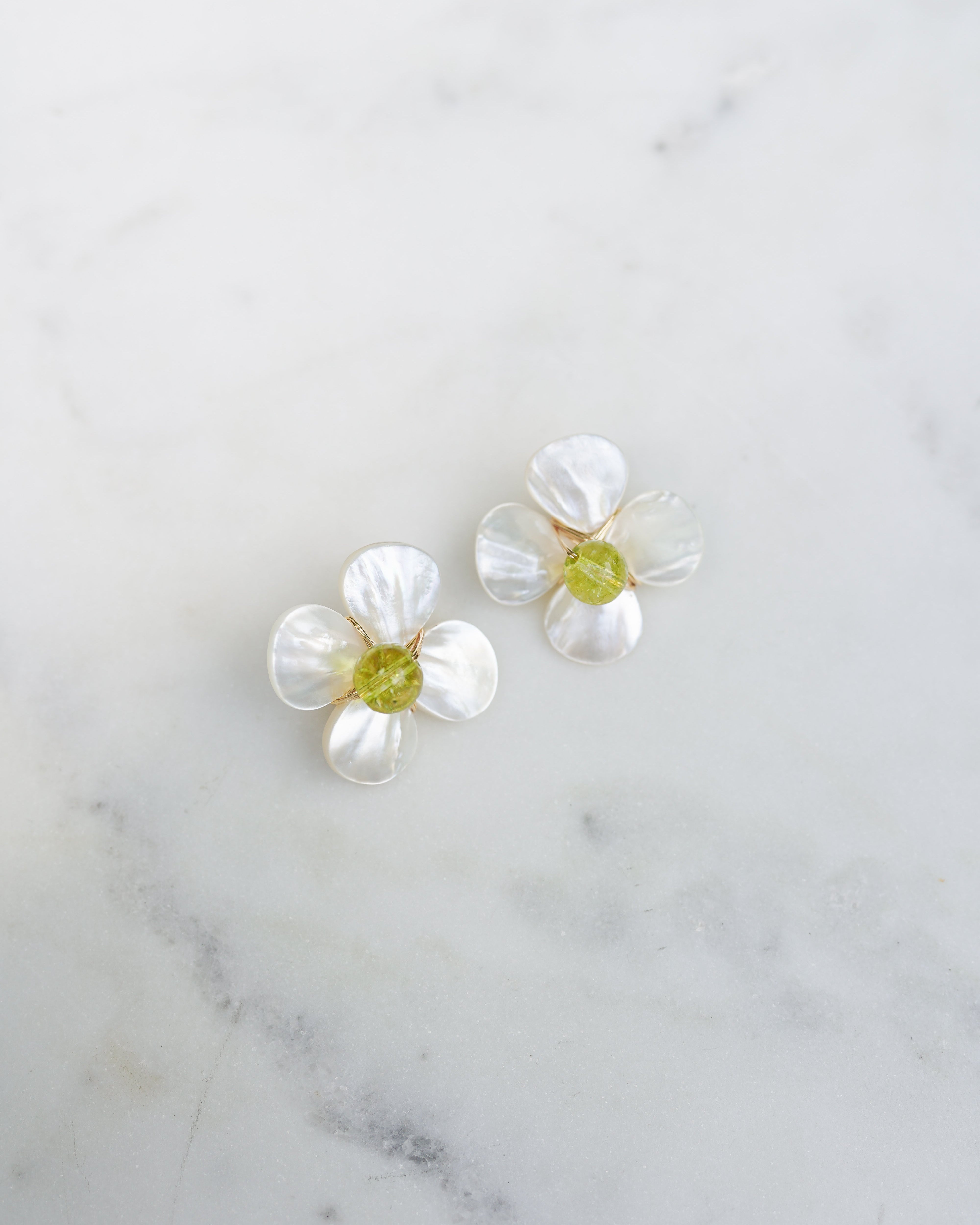 Pair of white floral earrings with green centers on a marble surface
