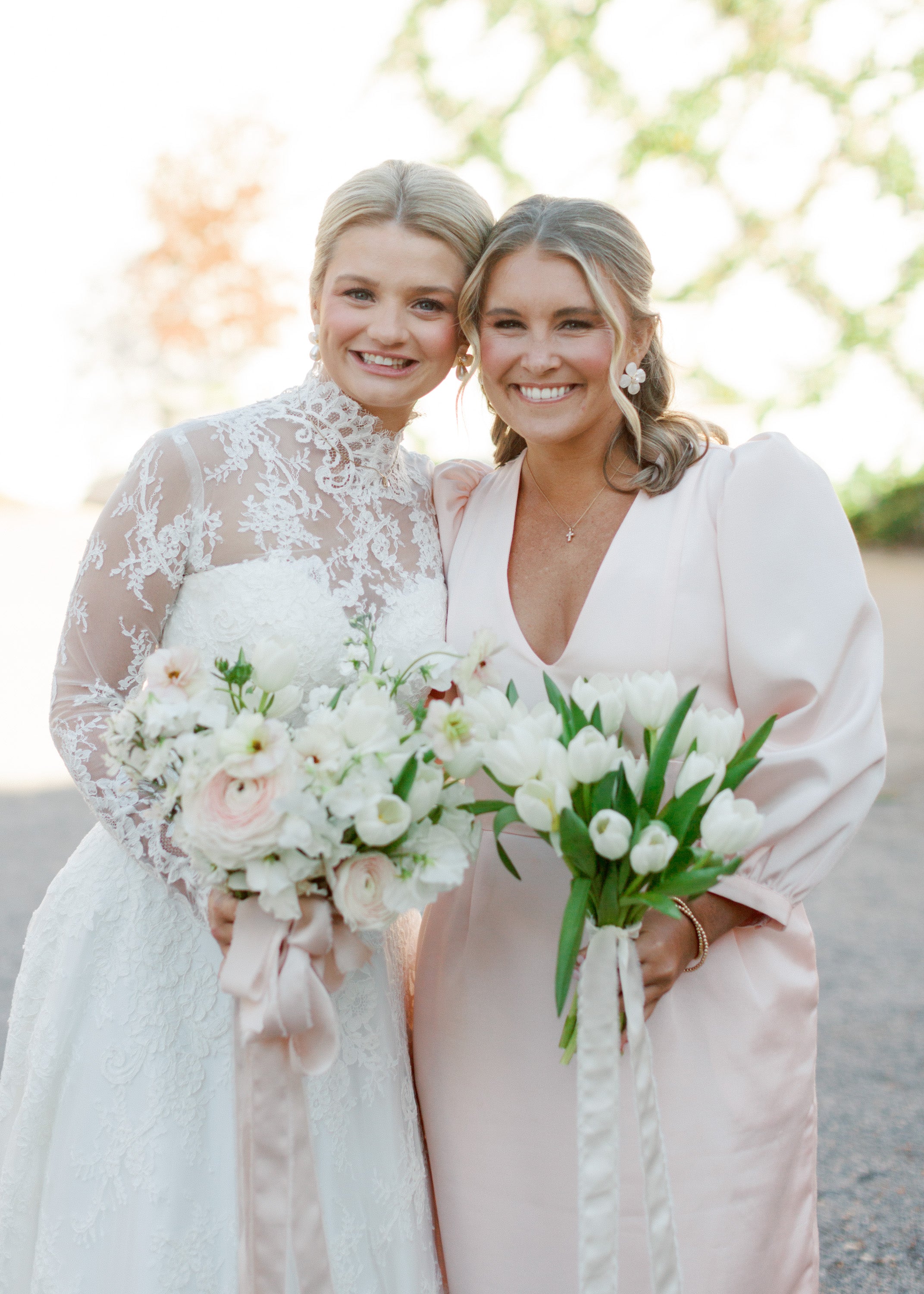 Two women in wedding attire holding bouquets outdoors.