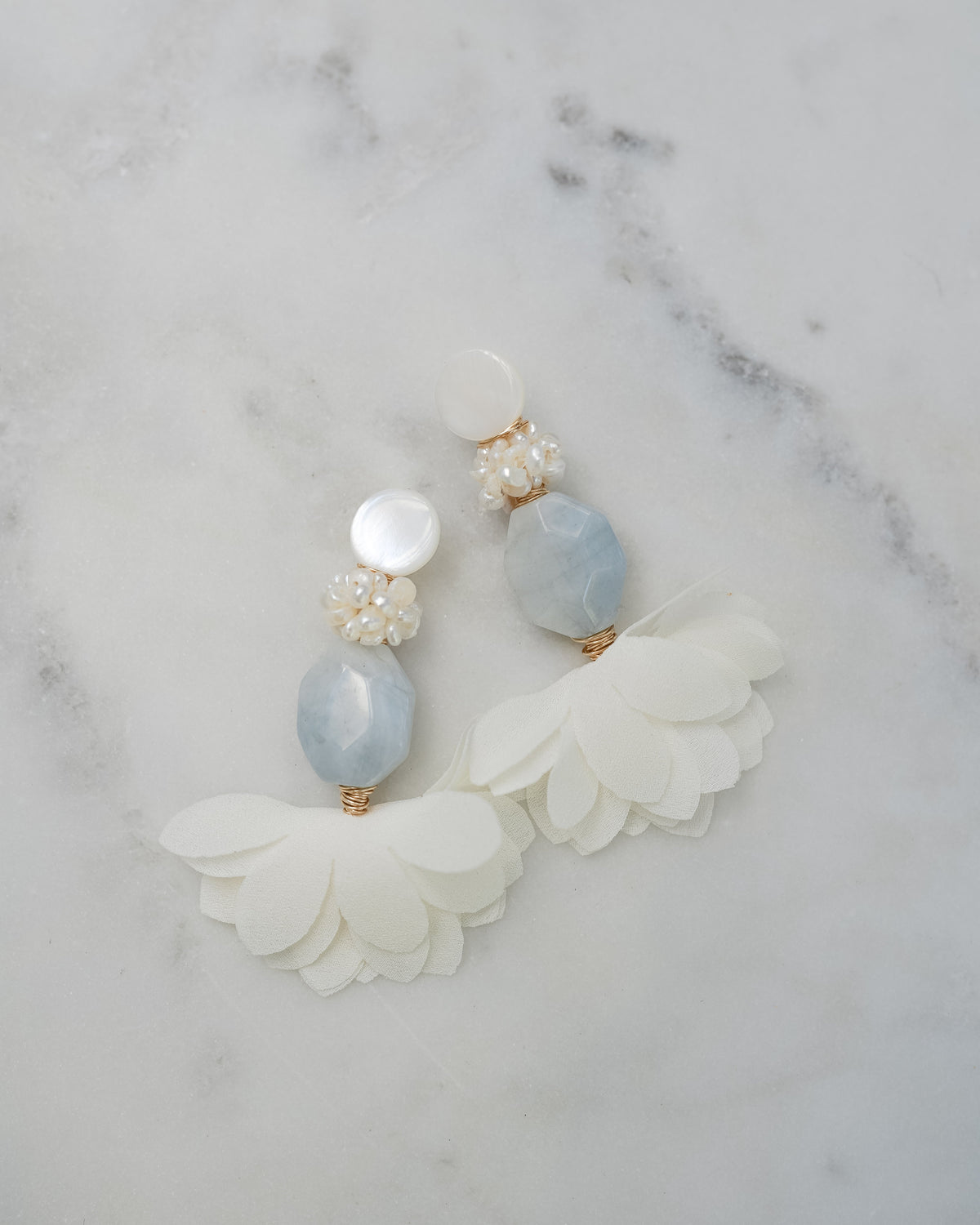 mother of pearl and aquamarine statement earrings on a white marble background