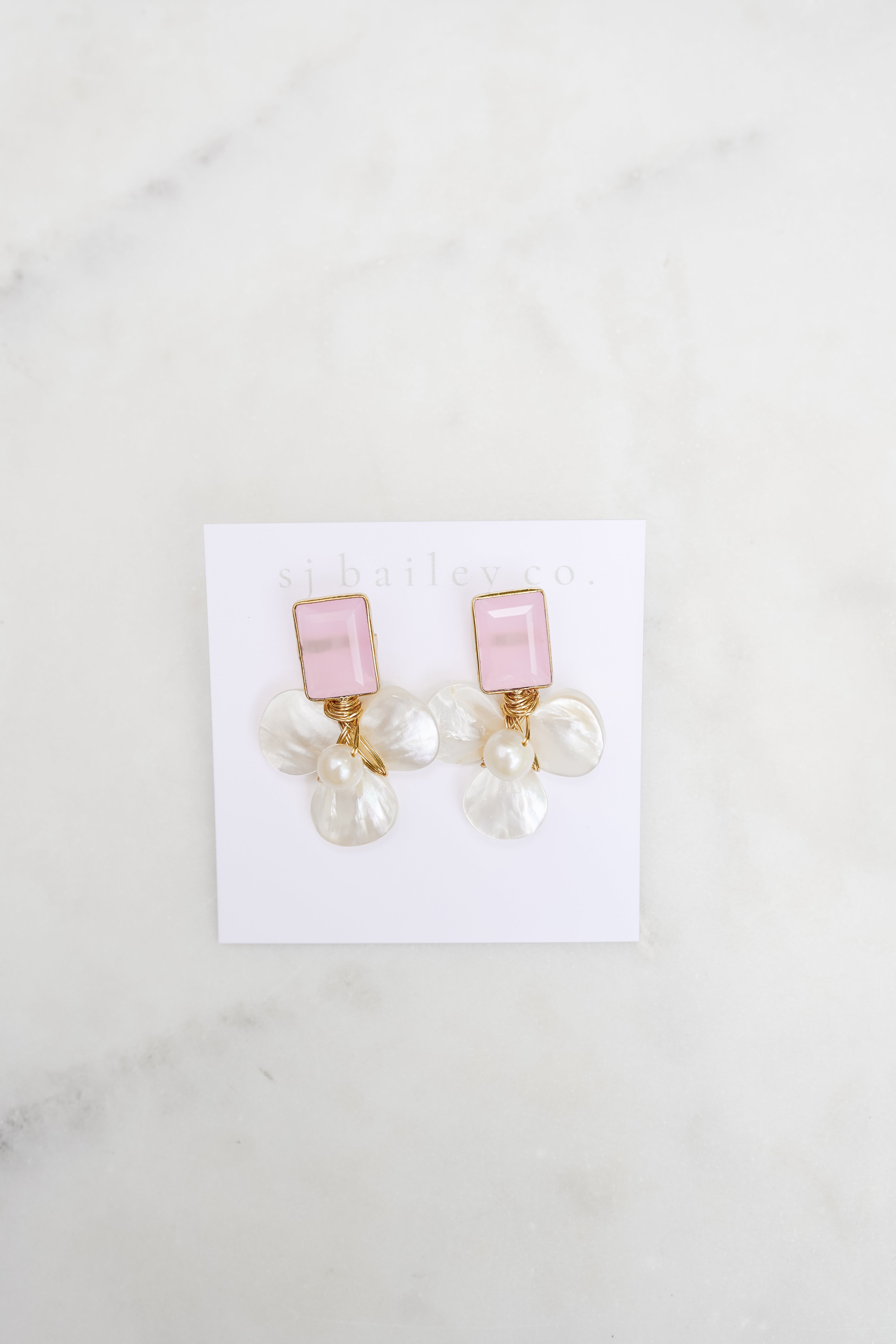 Pink stone and pearl earrings against a white marble background.