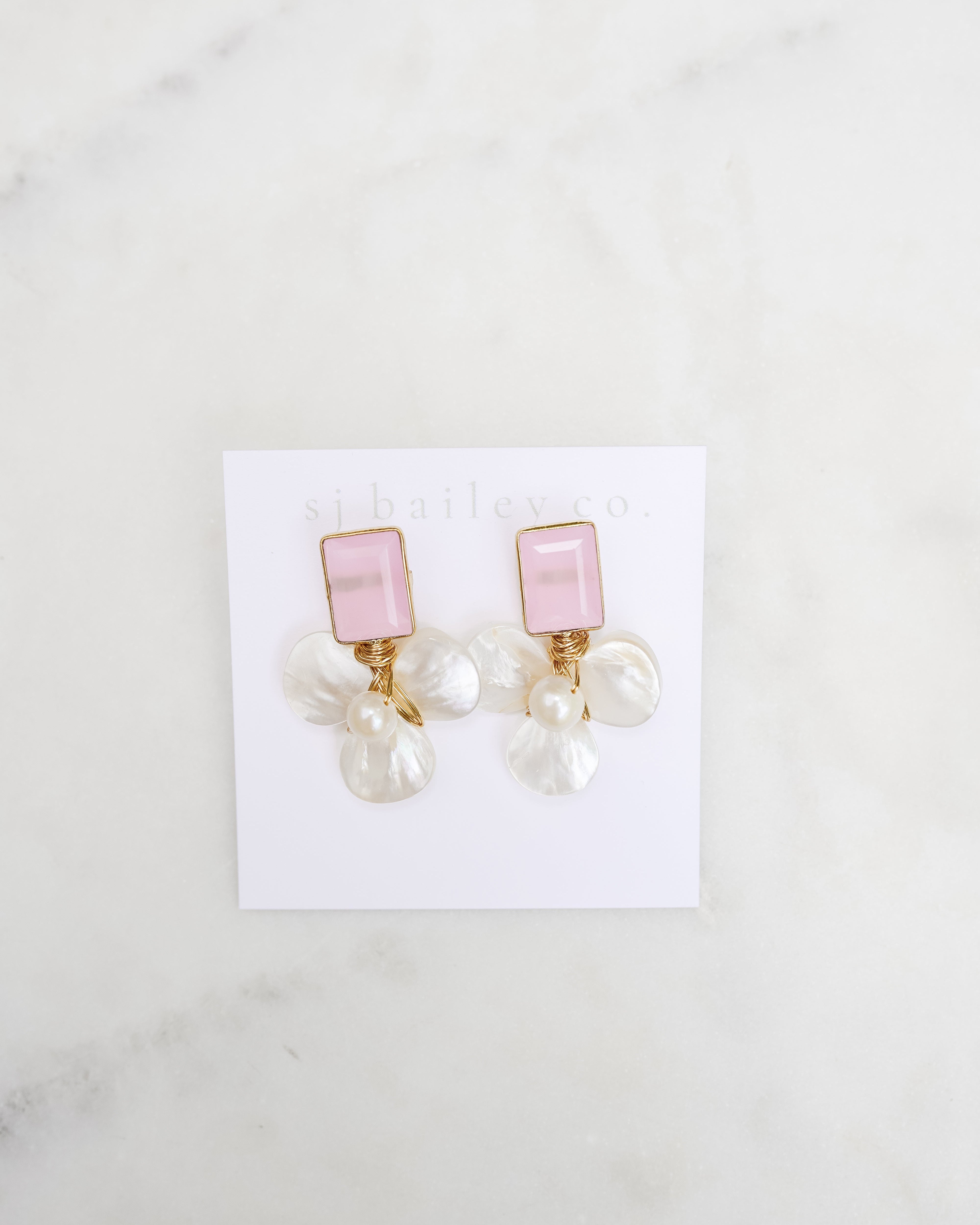 Pink stone and pearl earrings against a white marble background.