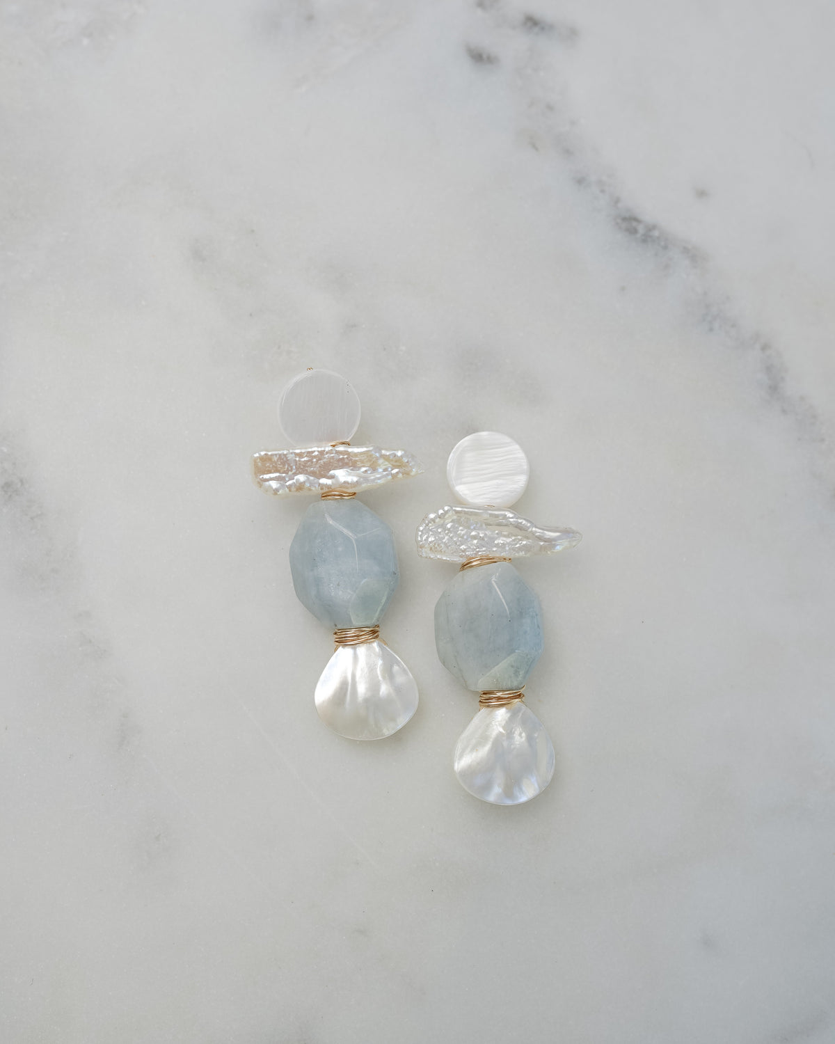 mother of pearl and aquamarine statement earrings on a white marble background