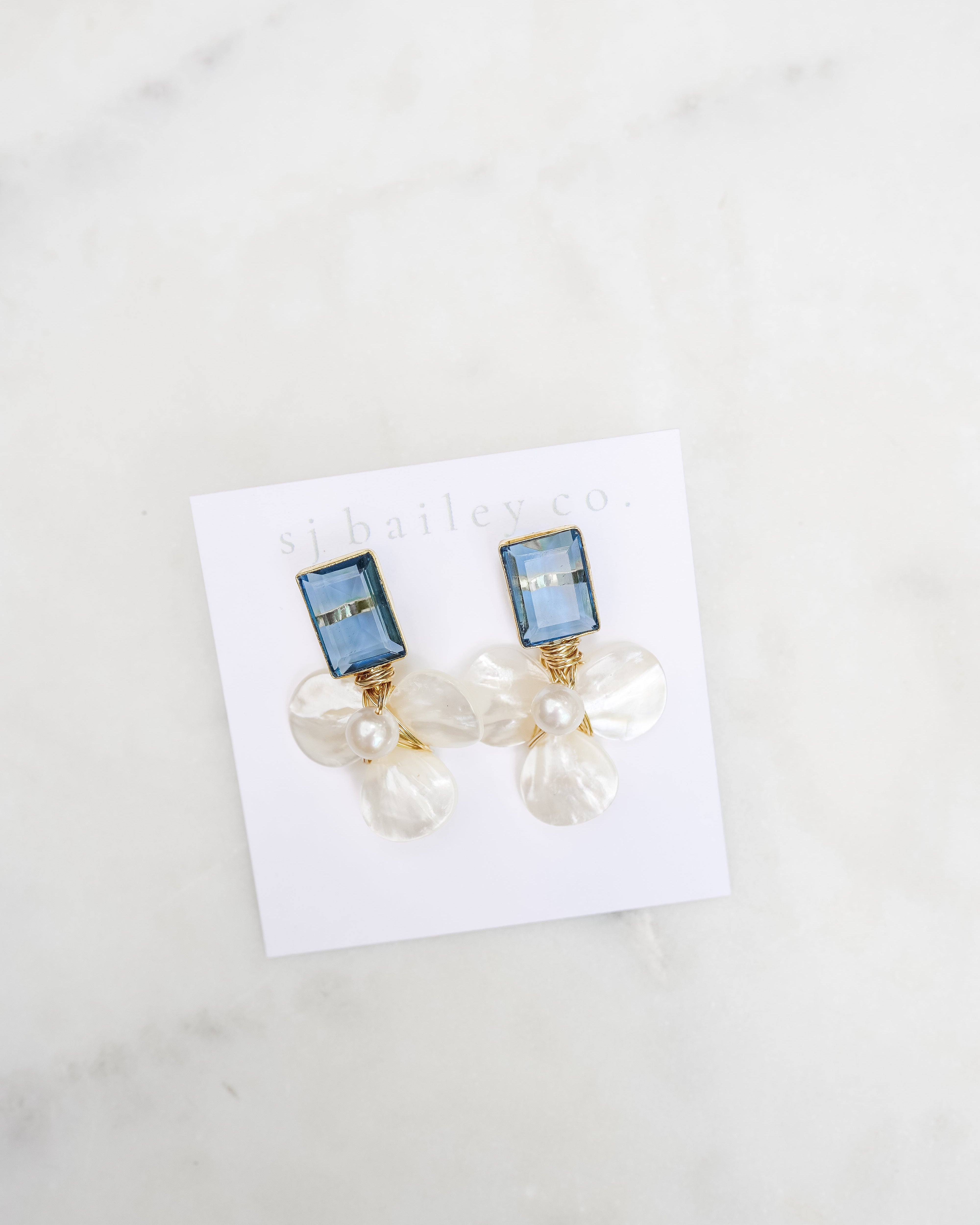 London blue and pearl floral earrings on a white card against a marble background