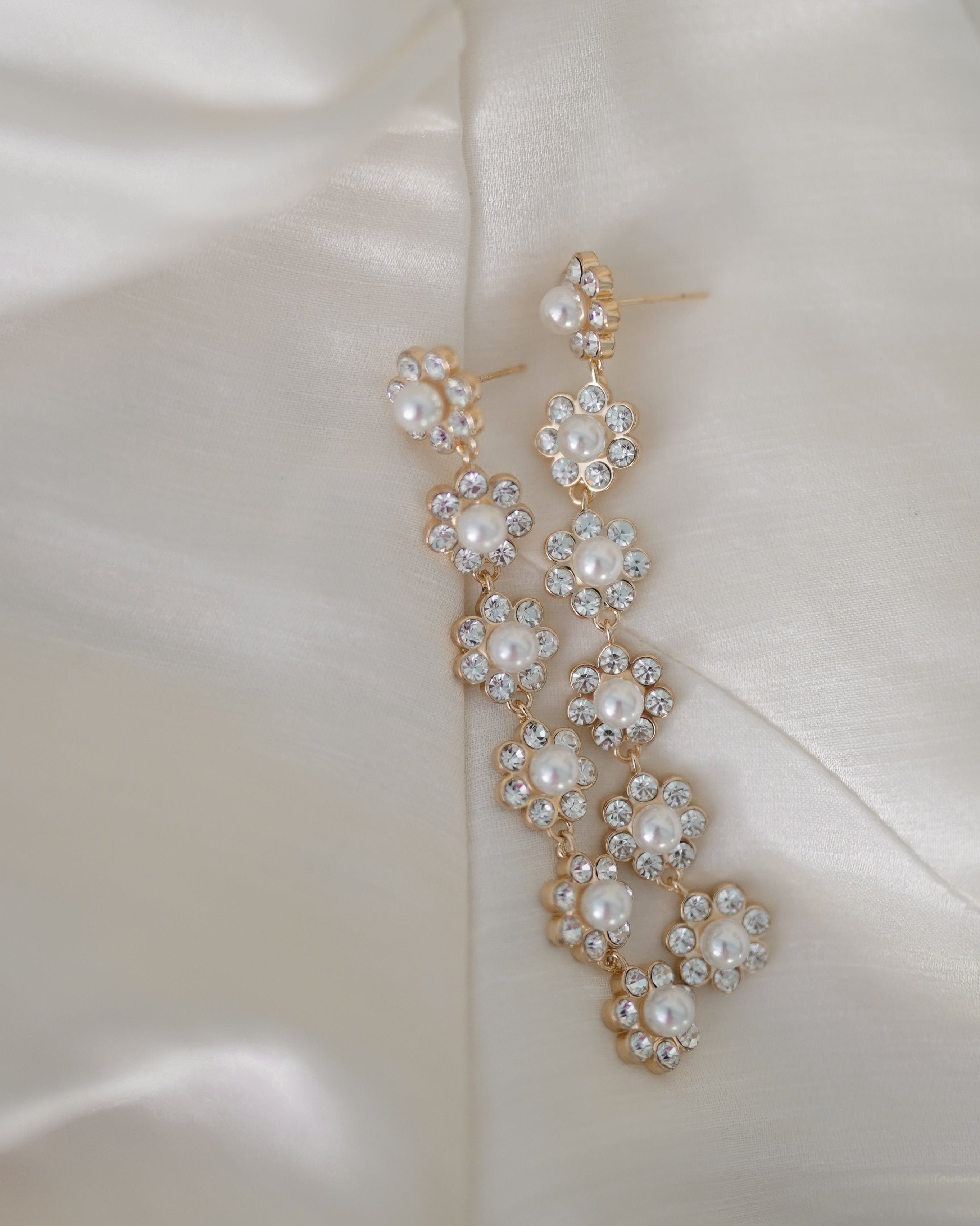 Crystal and pearl floral earrings on an ivory silk background