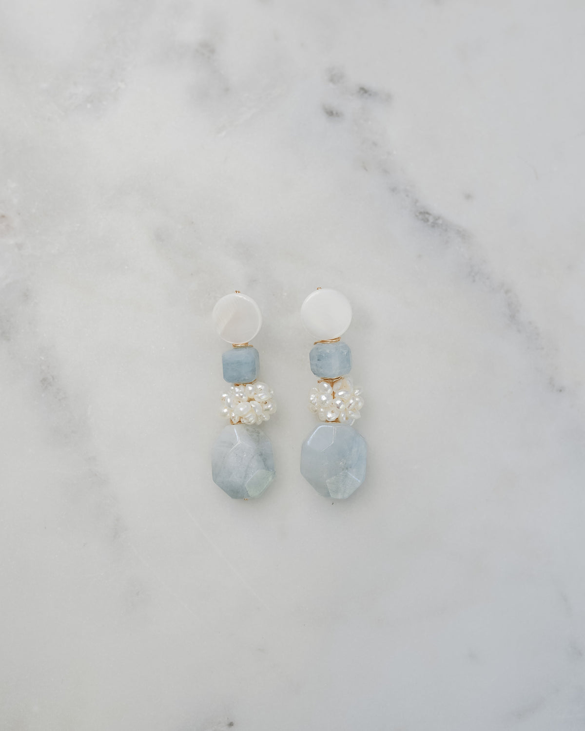 mother of pearl and aquamarine statement earrings on a white marble background