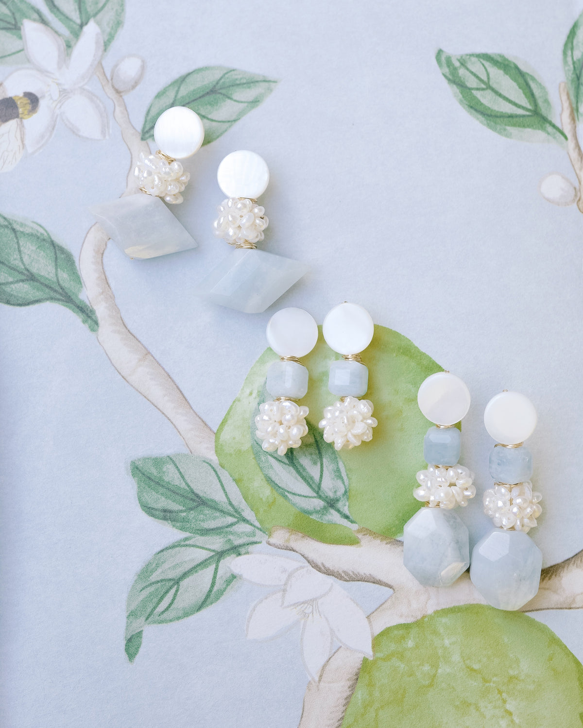 mother of pearl and aquamarine statement earrings on a blue floral background with green limes and leaves