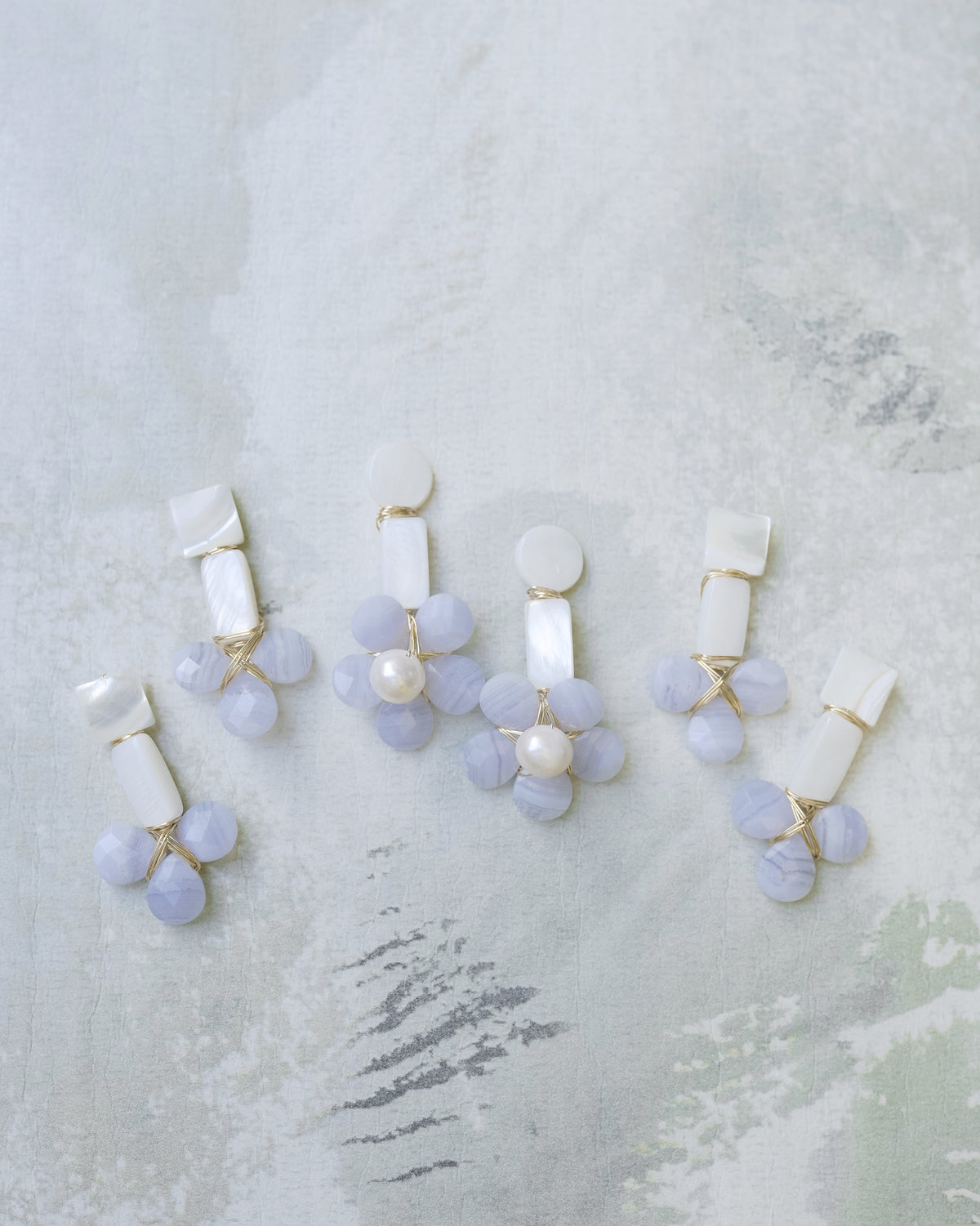 mother of pearl and blue lace agate stone statement earrings on a green floral background
