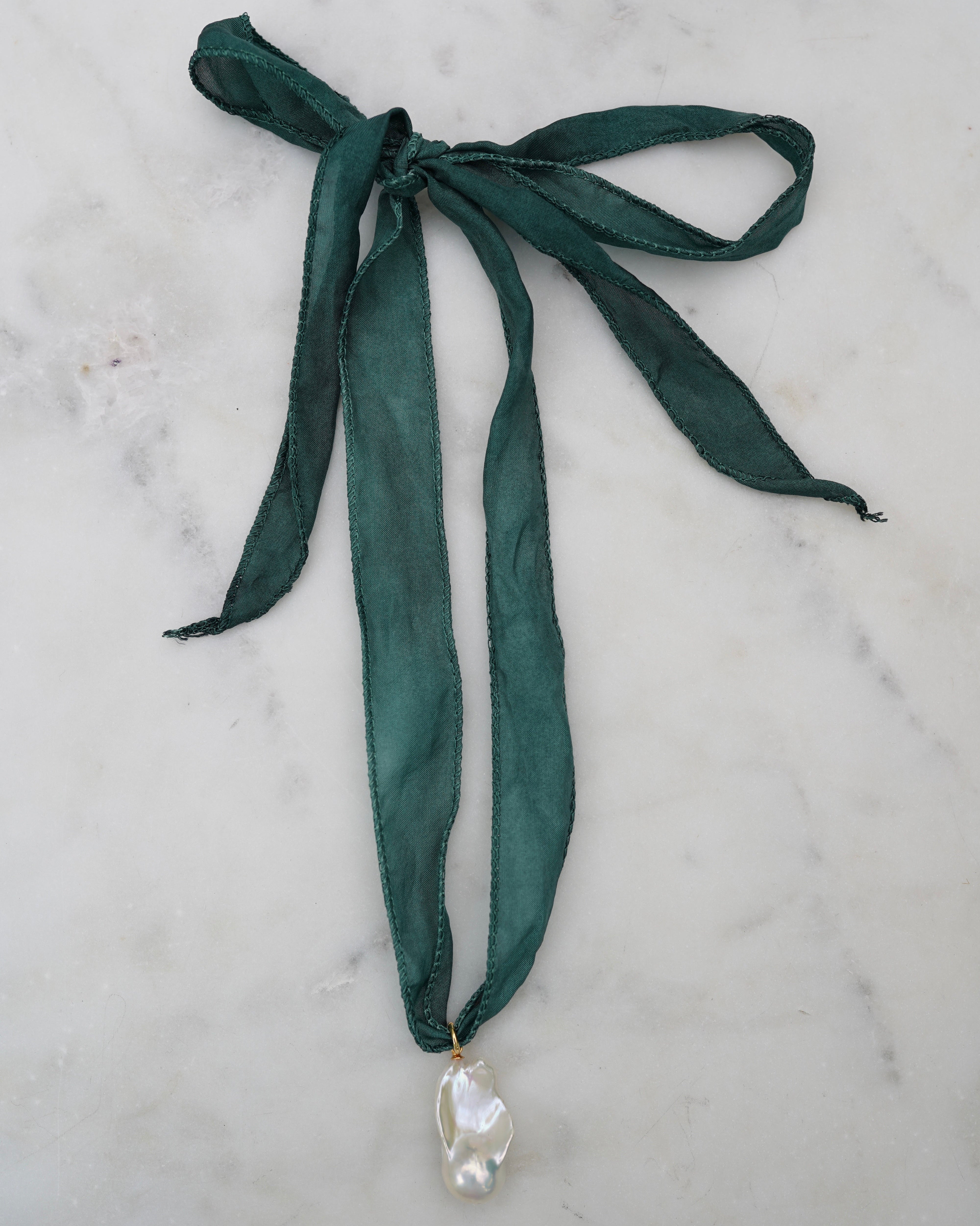 Green ribbon necklace with a pearl pendant on a marble surface