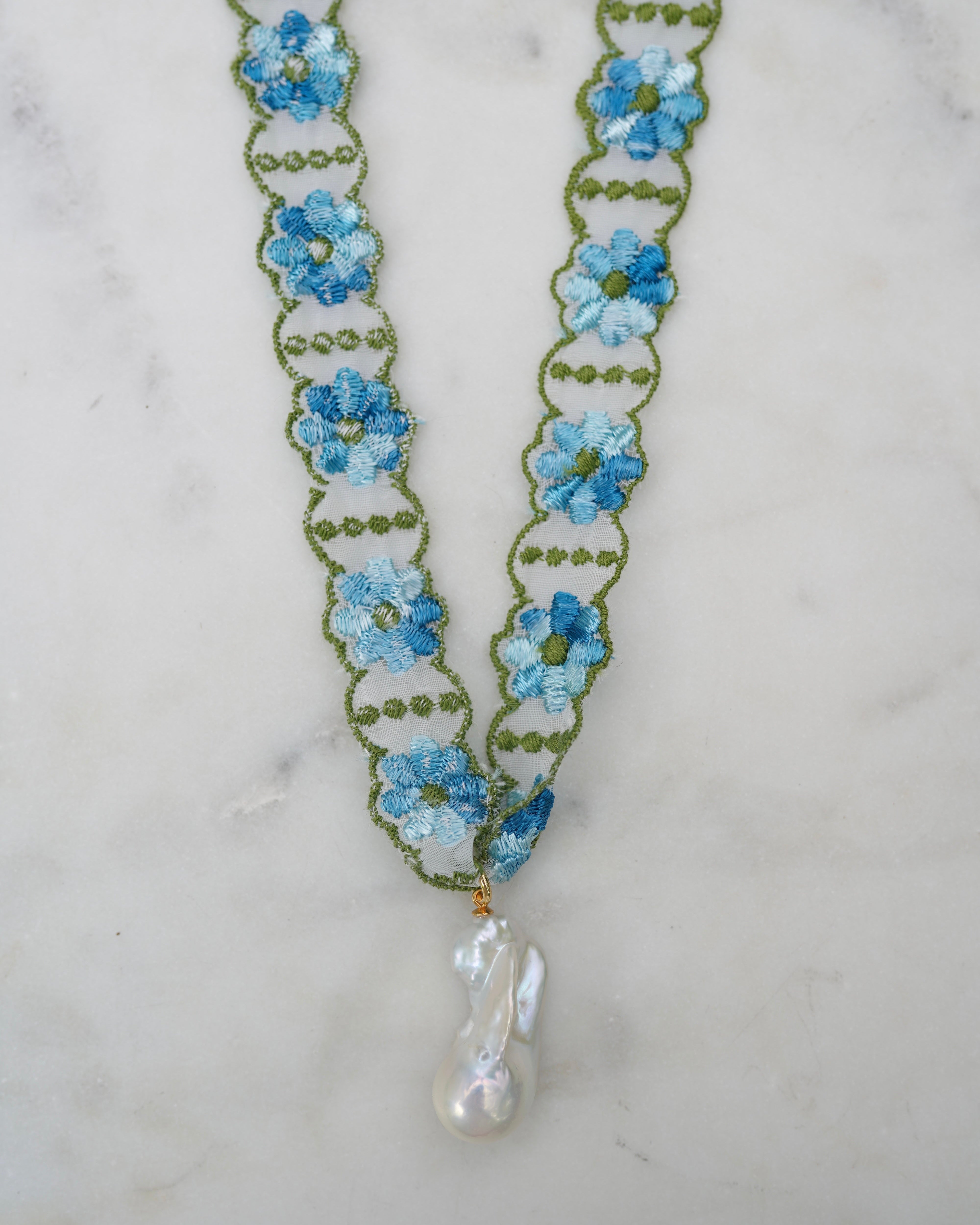 Floral necklace with blue flowers and a pearl drop on a marble background