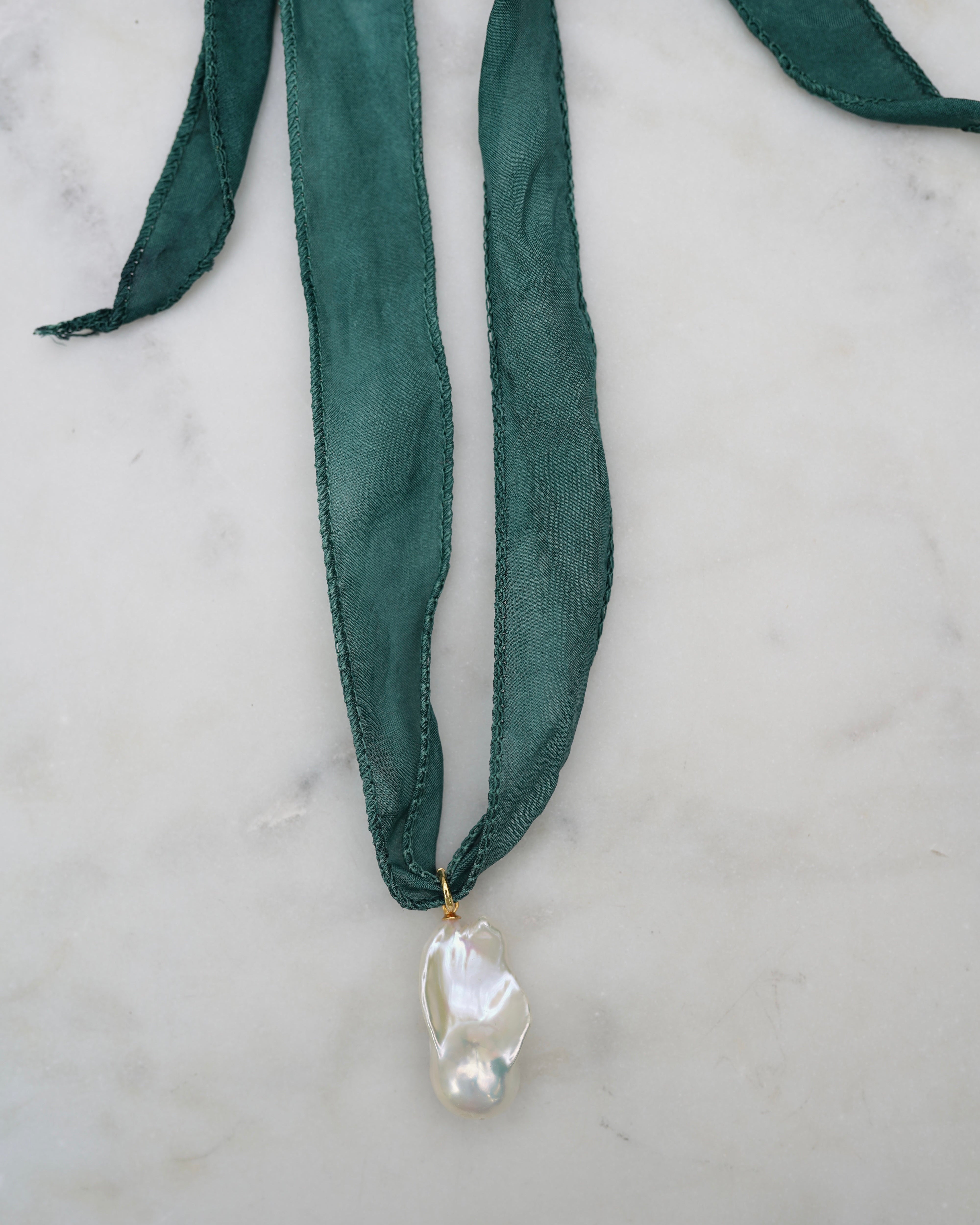 Green ribbon necklace with a pearl pendant on a marble surface