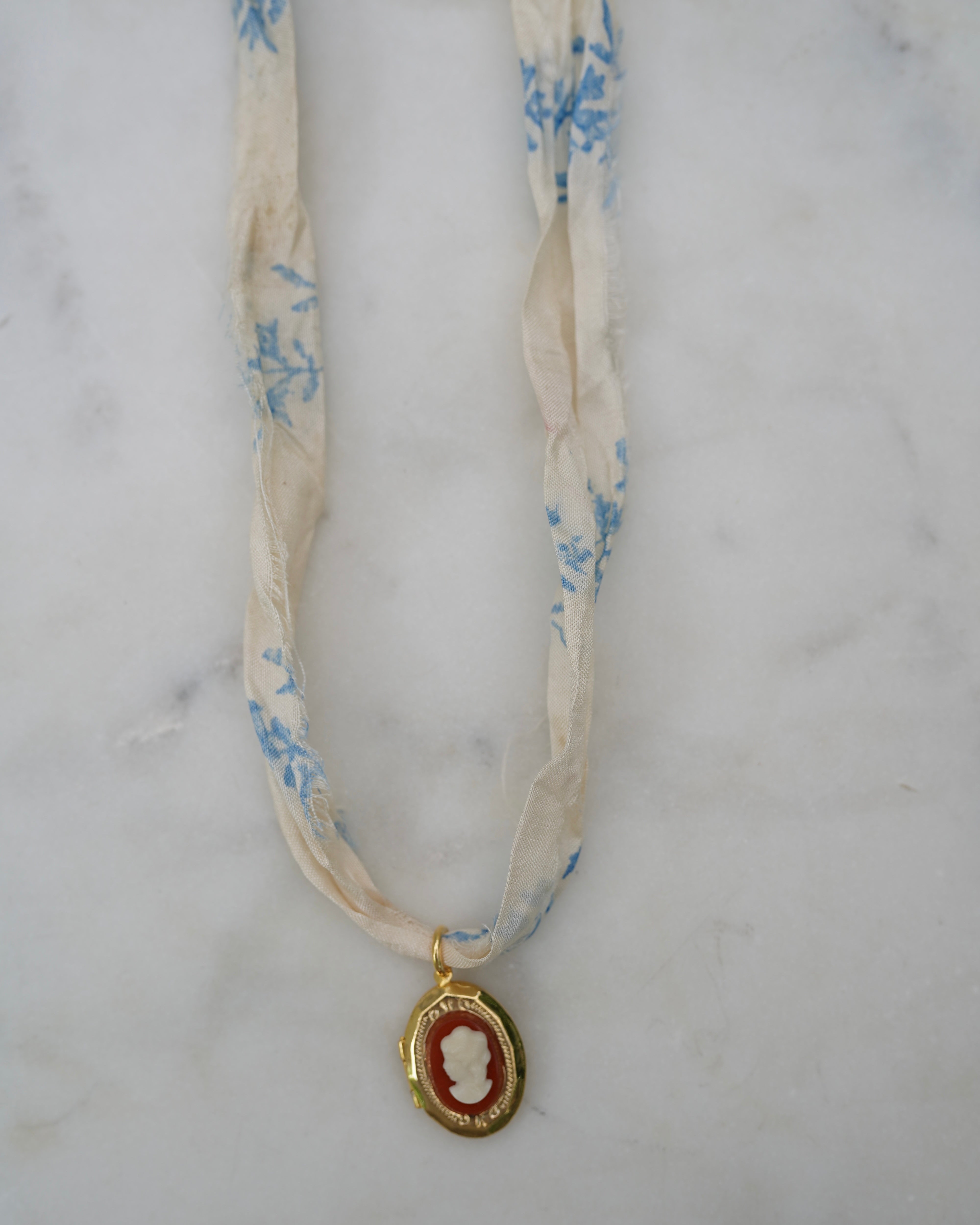 Necklace with a cameo pendant on a floral ribbon against a marble background