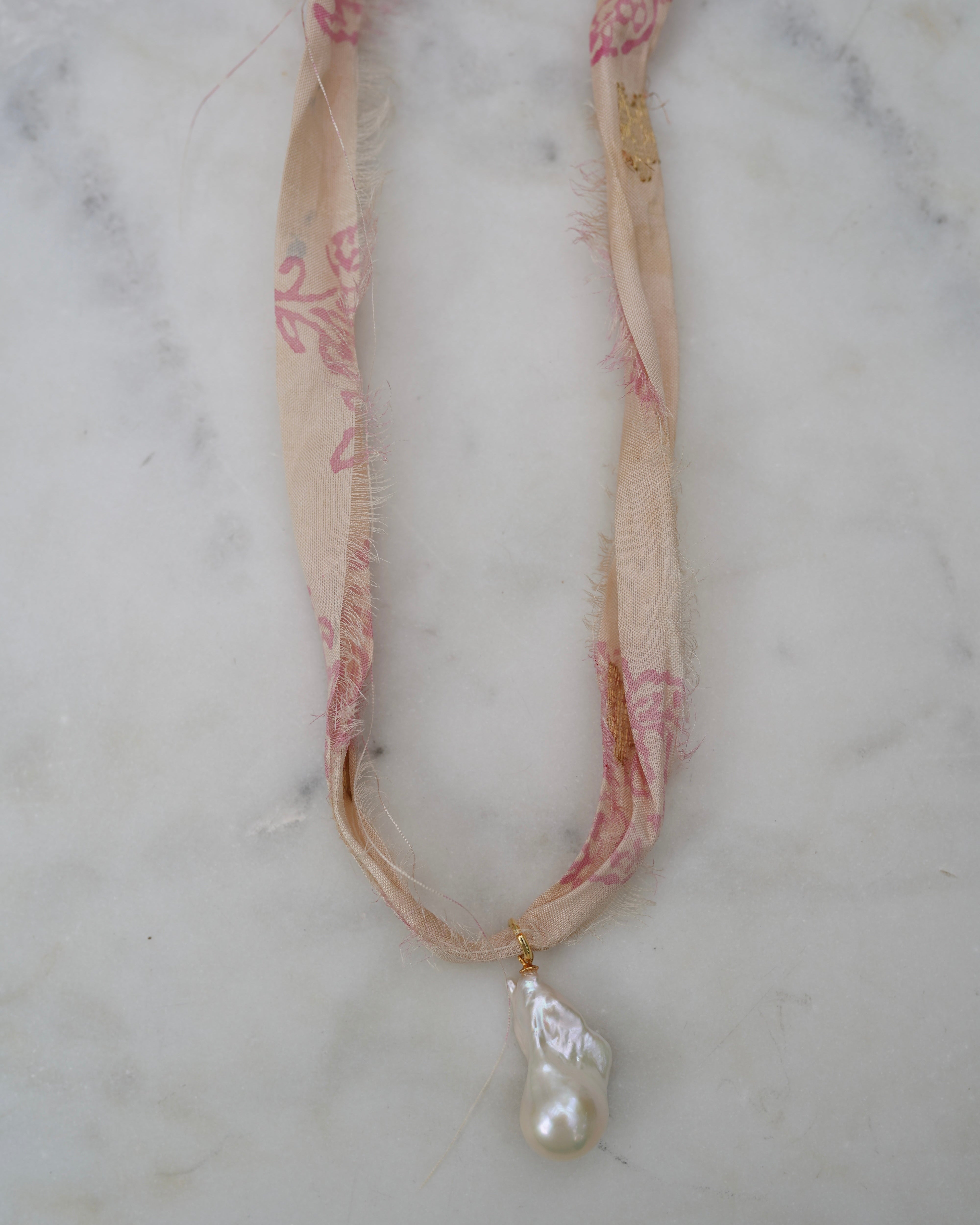 Necklace with pink floral patterned strap and pearl pendant on a marble surface