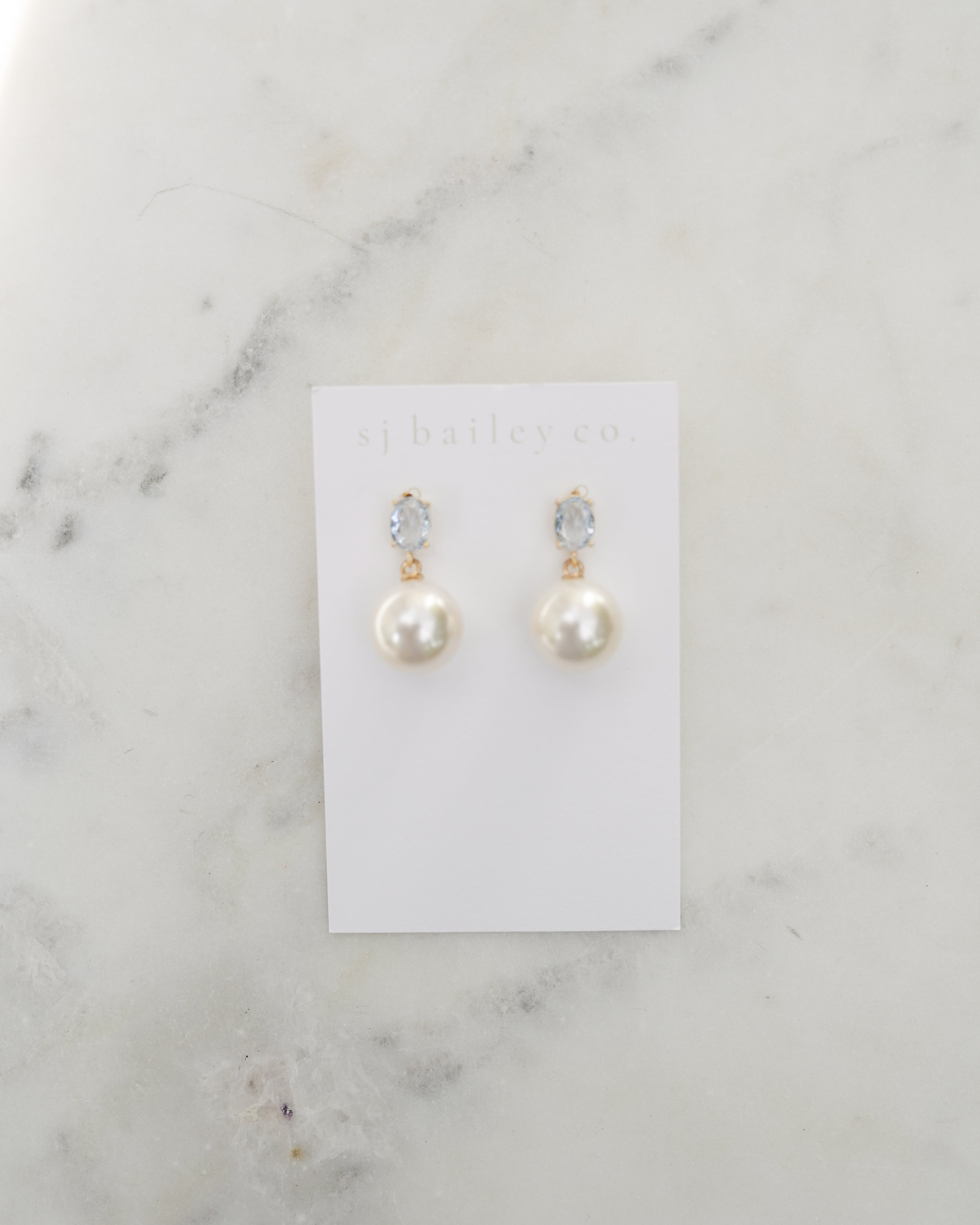 Pair of pearl earrings on a display card against a marble background