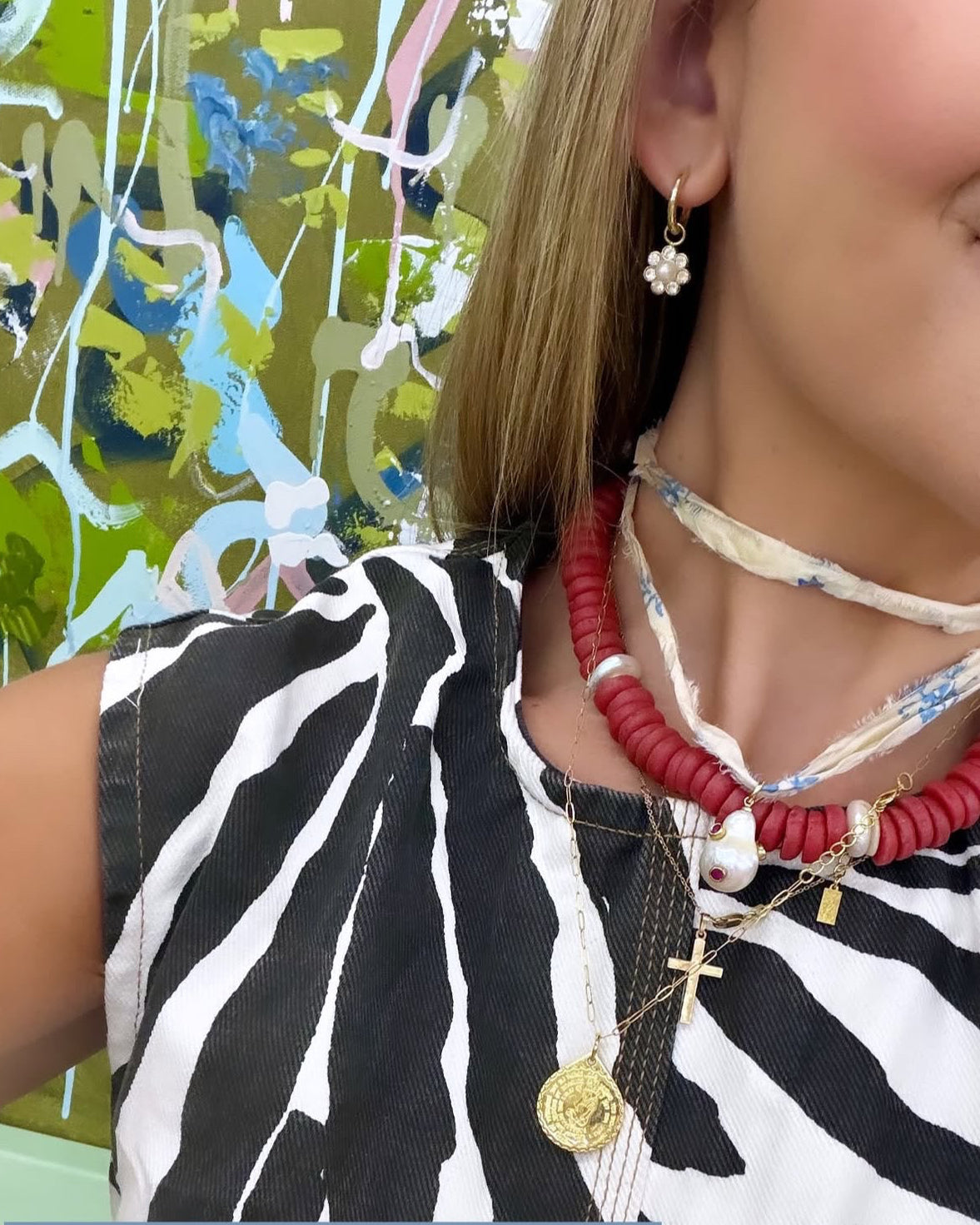 Person wearing a zebra print top with jewelry, including necklaces and earrings, against a colorful abstract background.