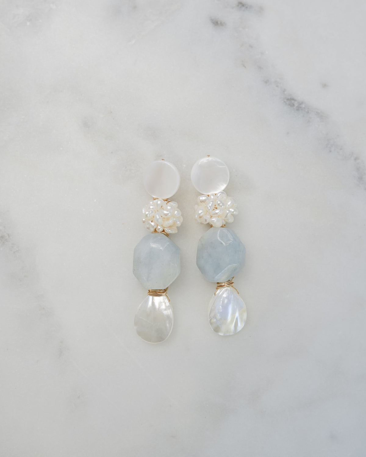 mother of pearl and aquamarine statement earrings on a white marble background