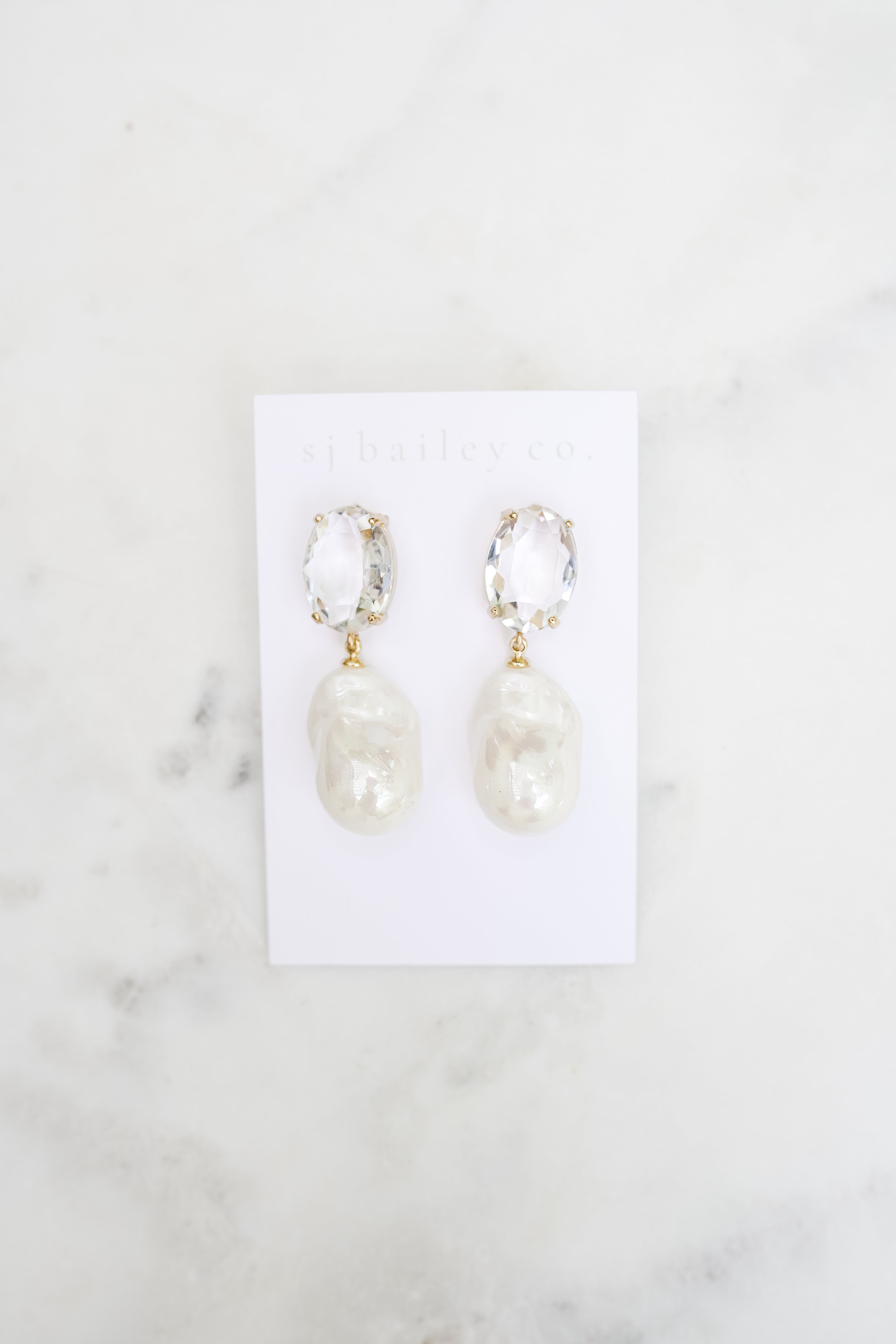 Crystal Oval and pearl pendant earrings on a white marble background. 
