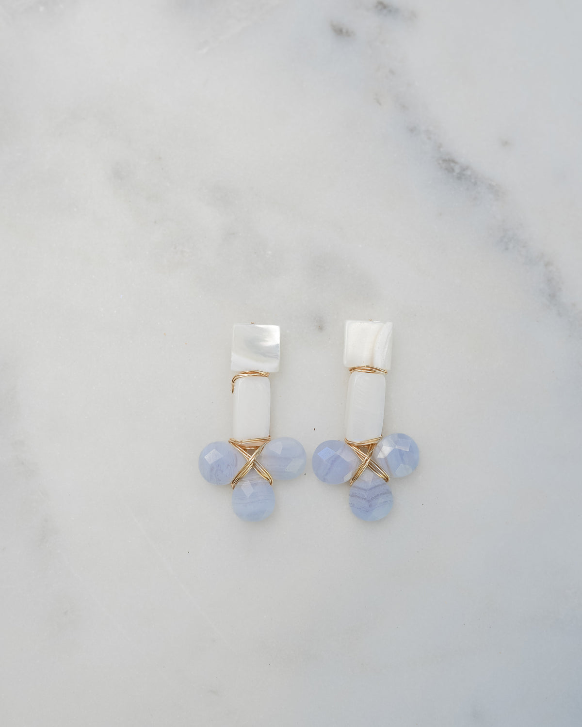 mother of pearl and blue lace agate statement earrings on a white marble background