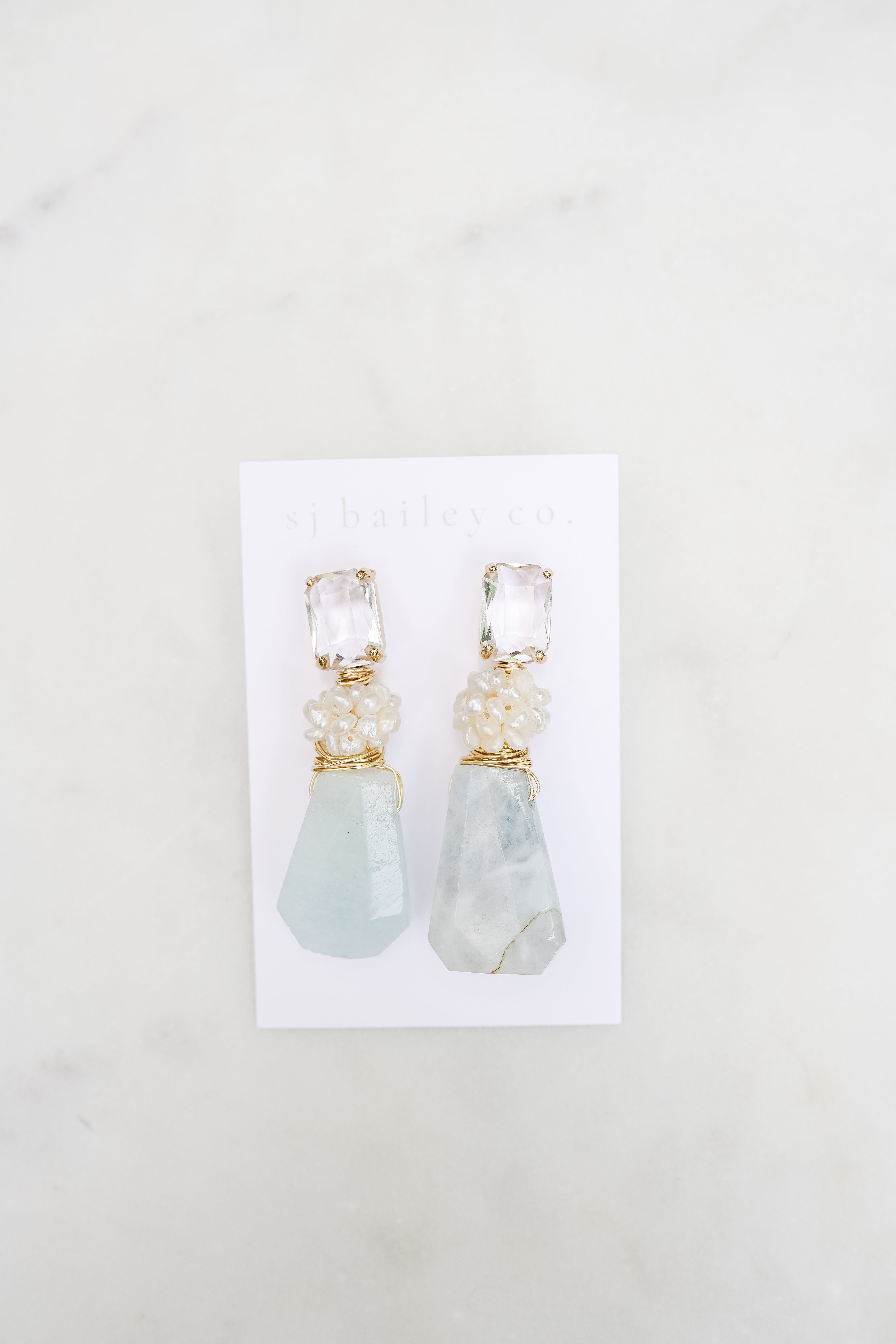 Pearl cluster and aquamarine statement earrings on a white card against a marble background. 