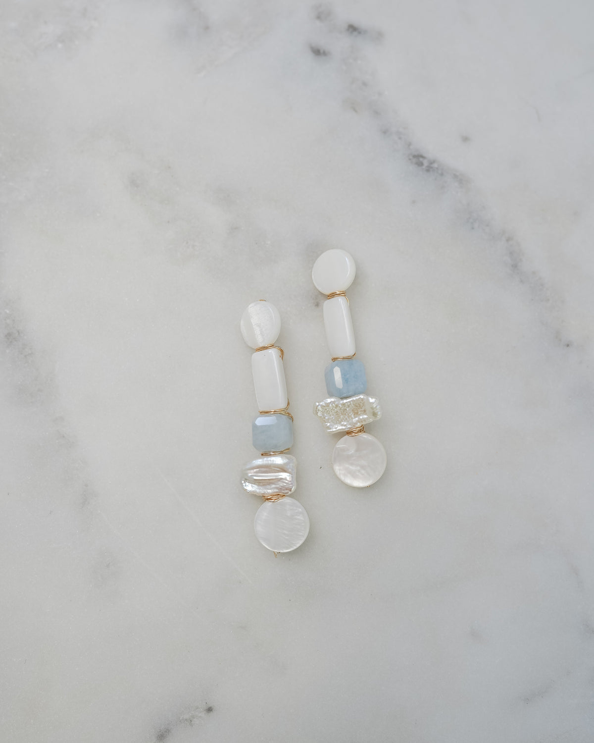 mother of pearl and aquamarine statement earrings on a white marble background