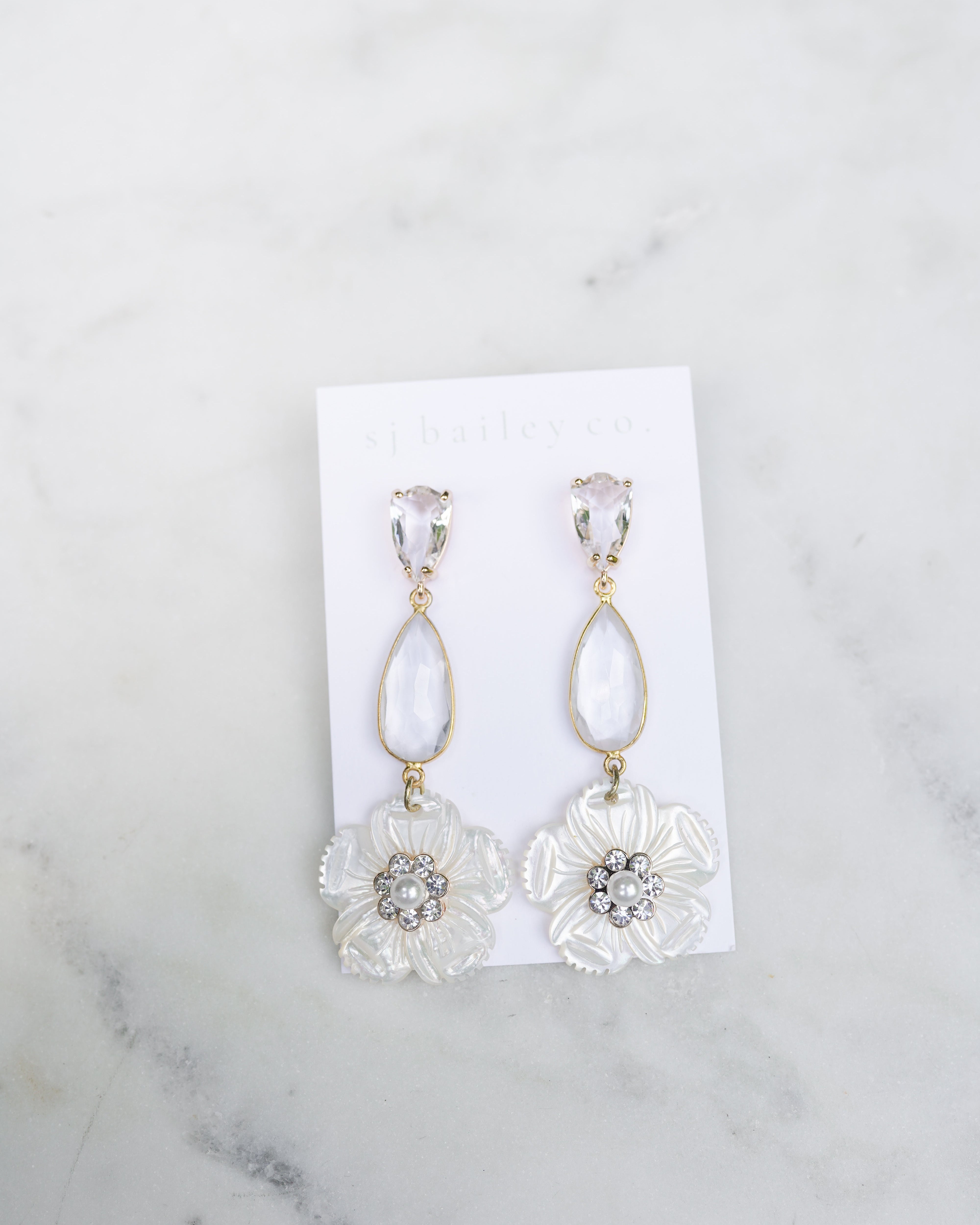 Pair of floral earrings on a white card against a marble background