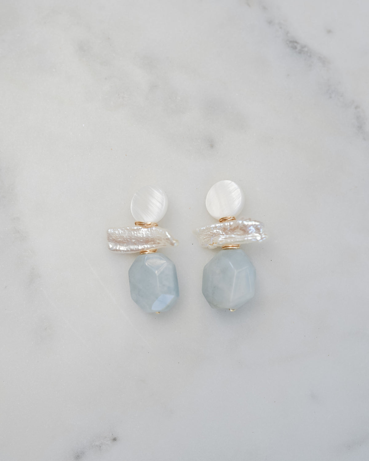 mother of pearl and aquamarine statement earrings on a white marble background
