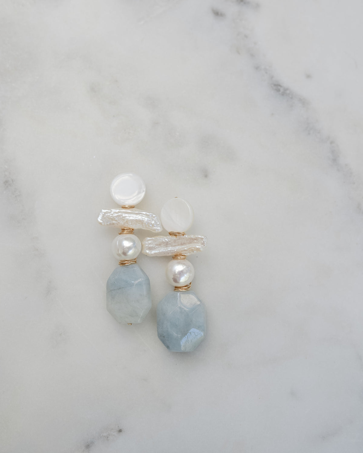 mother of pearl and aquamarine statement earrings on a white marble background