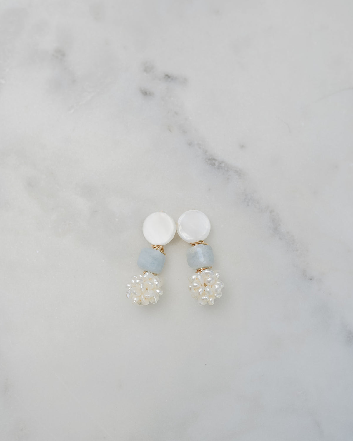 mother of pearl and aquamarine statement earrings on a white marble background