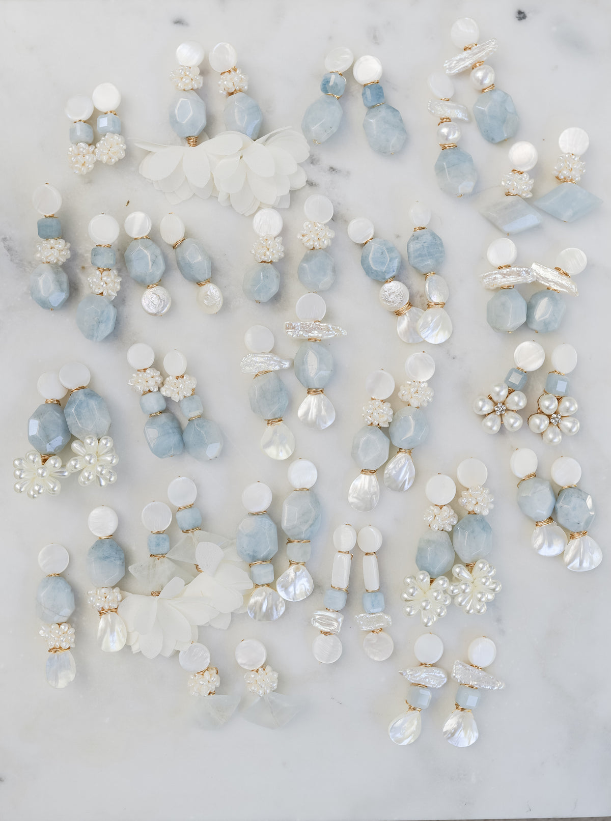 several statement pairs of mother of pearl and aquamarine earrings on a white marble background 