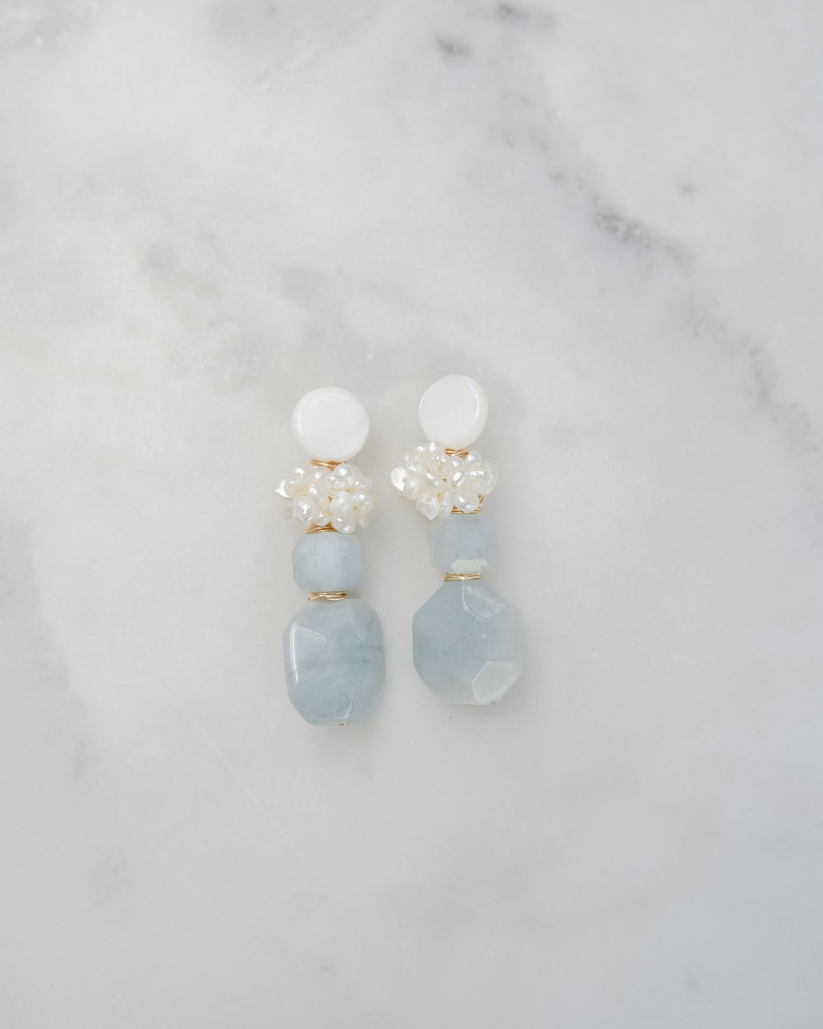 mother of pearl and aquamarine statement earrings on a white marble background