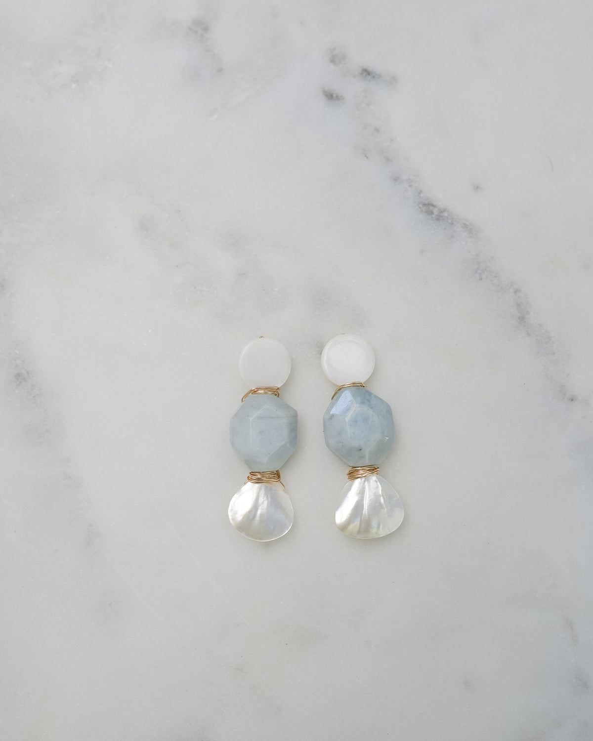 mother of pearl and aquamarine statement earrings on a white marble background