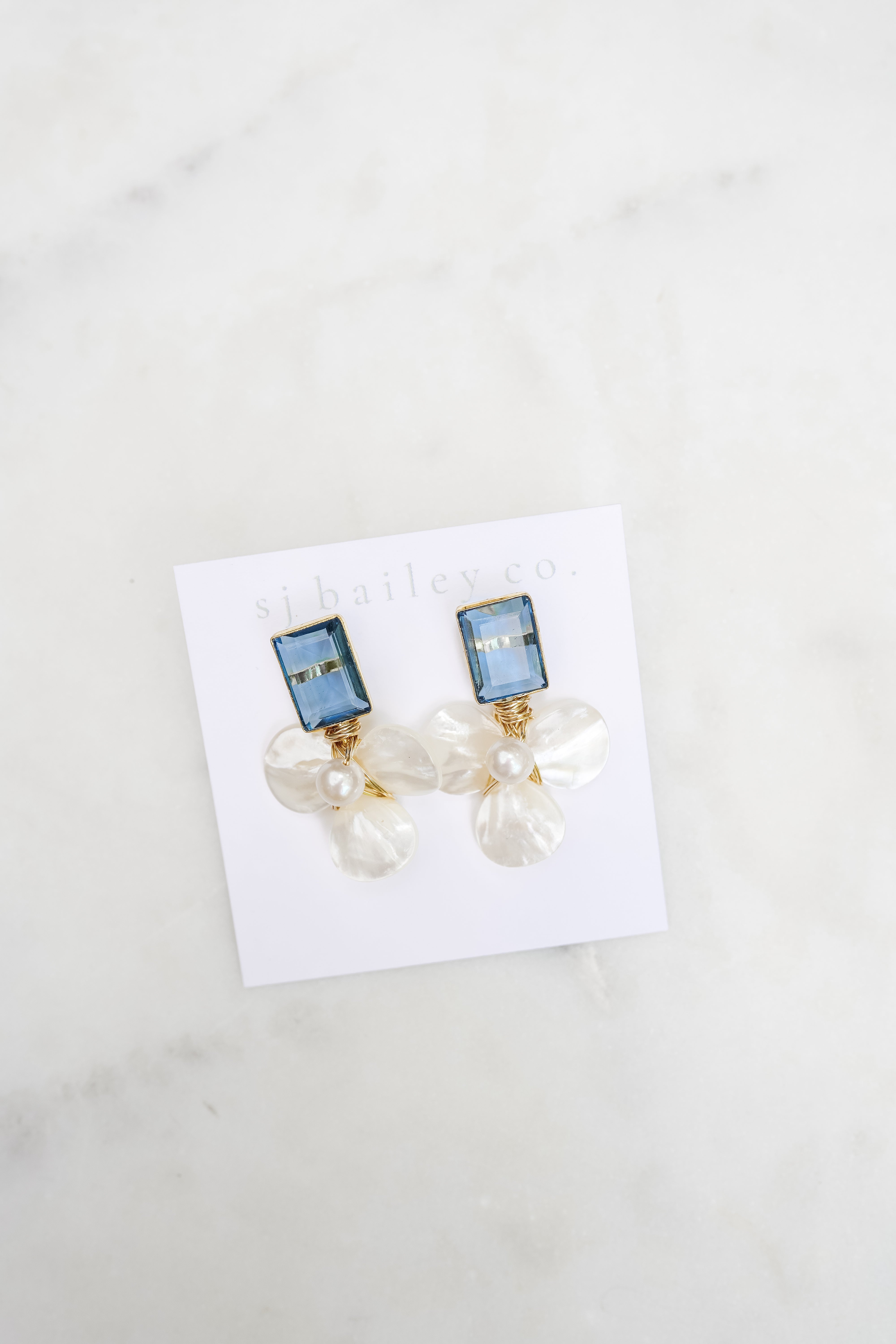 London blue and pearl floral earrings on a white card against a marble background 