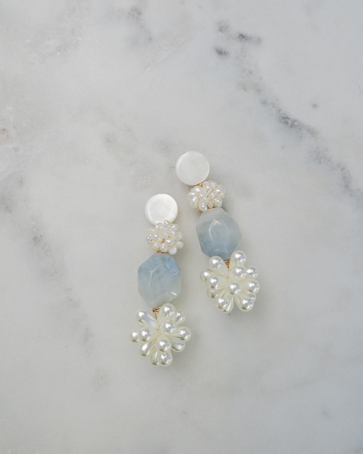 mother of pearl and aquamarine statement earrings on a white marble background